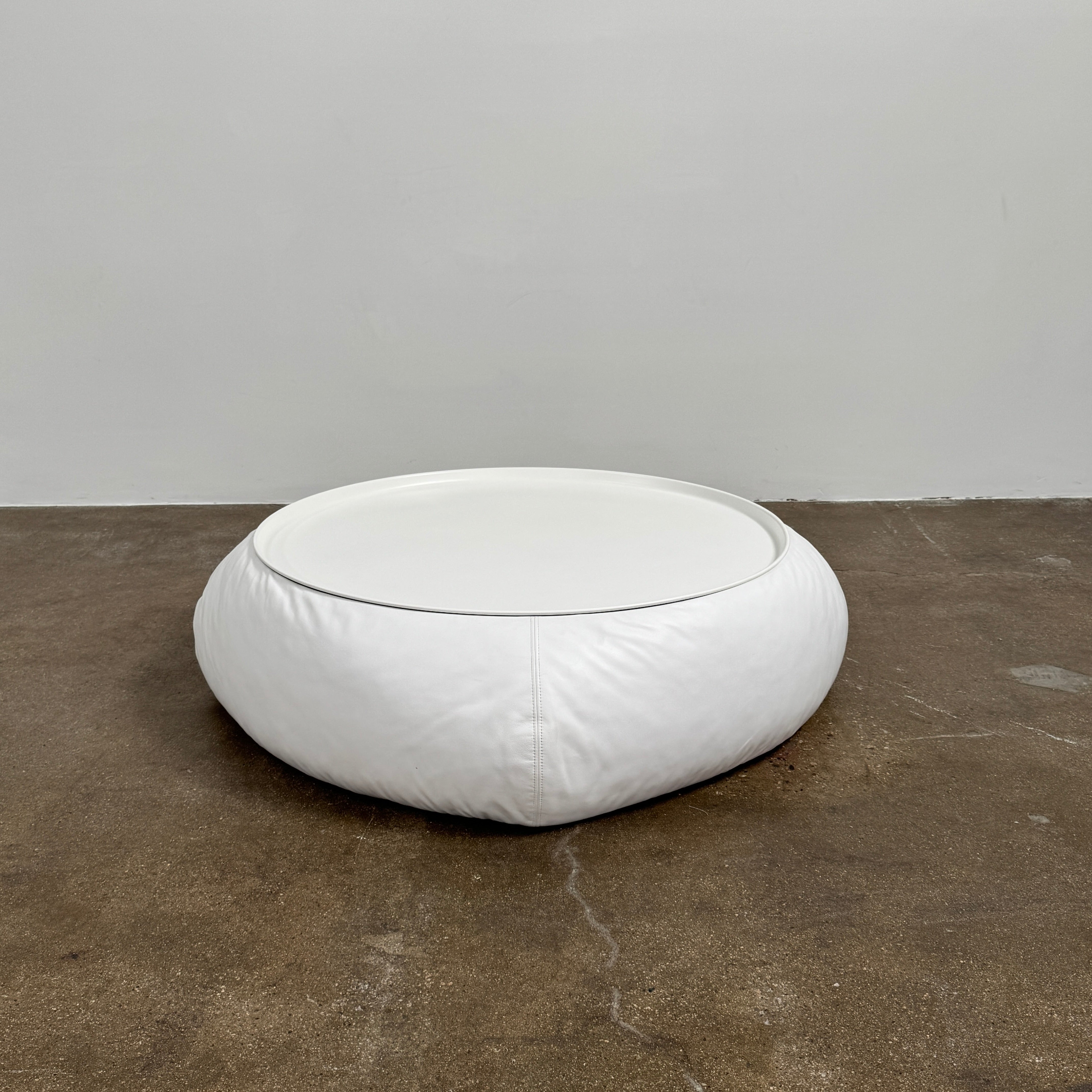 The B&B Italia Lady Fat Coffee Table by B&B Italia, a low, round table with a flat white top inspired by Patricia Urquiola’s design, sits on a plain brown floor against a light gray wall.