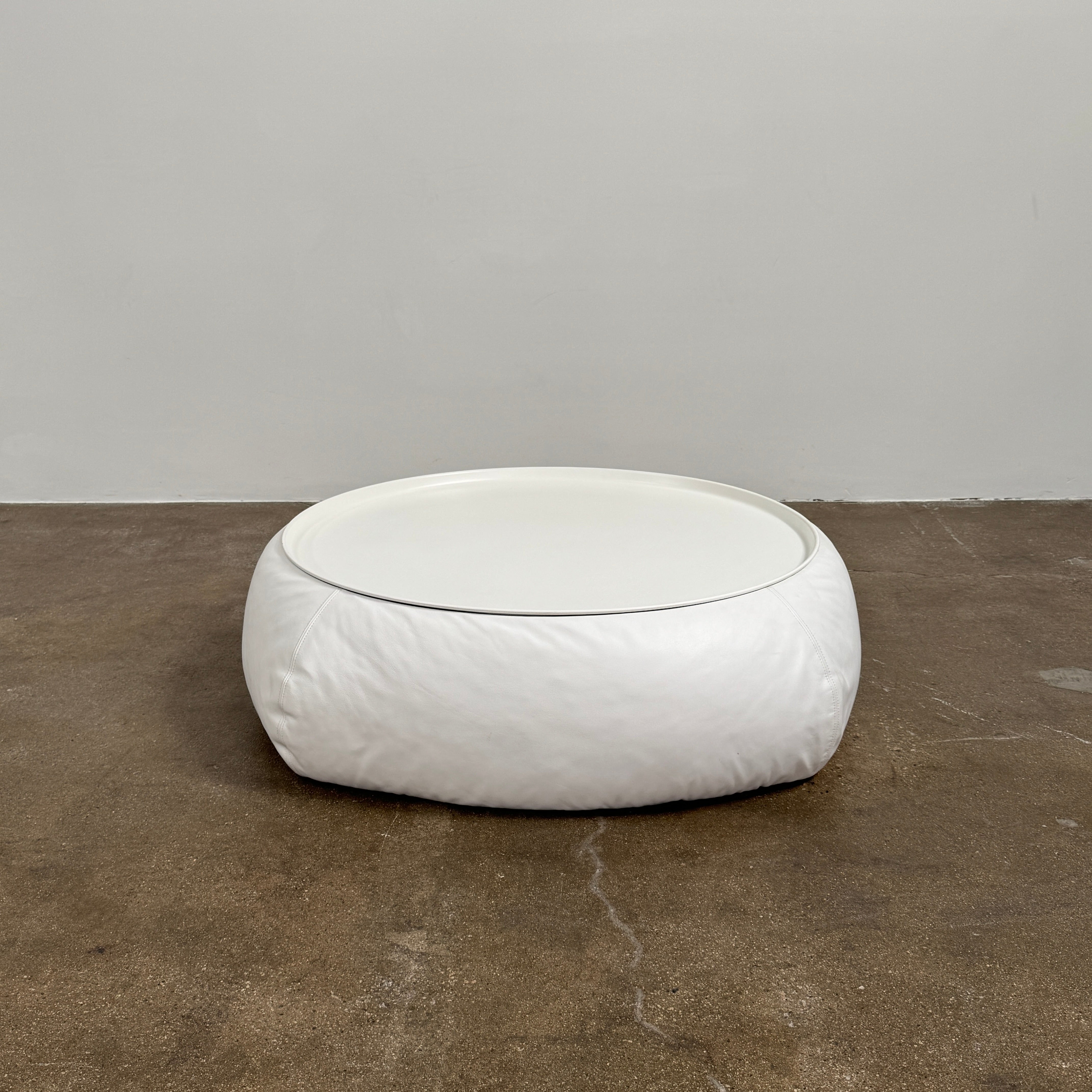 The B&B Italia Lady Fat Coffee Table by B&B Italia, a low, round table with a flat white top inspired by Patricia Urquiola’s design, sits on a plain brown floor against a light gray wall.