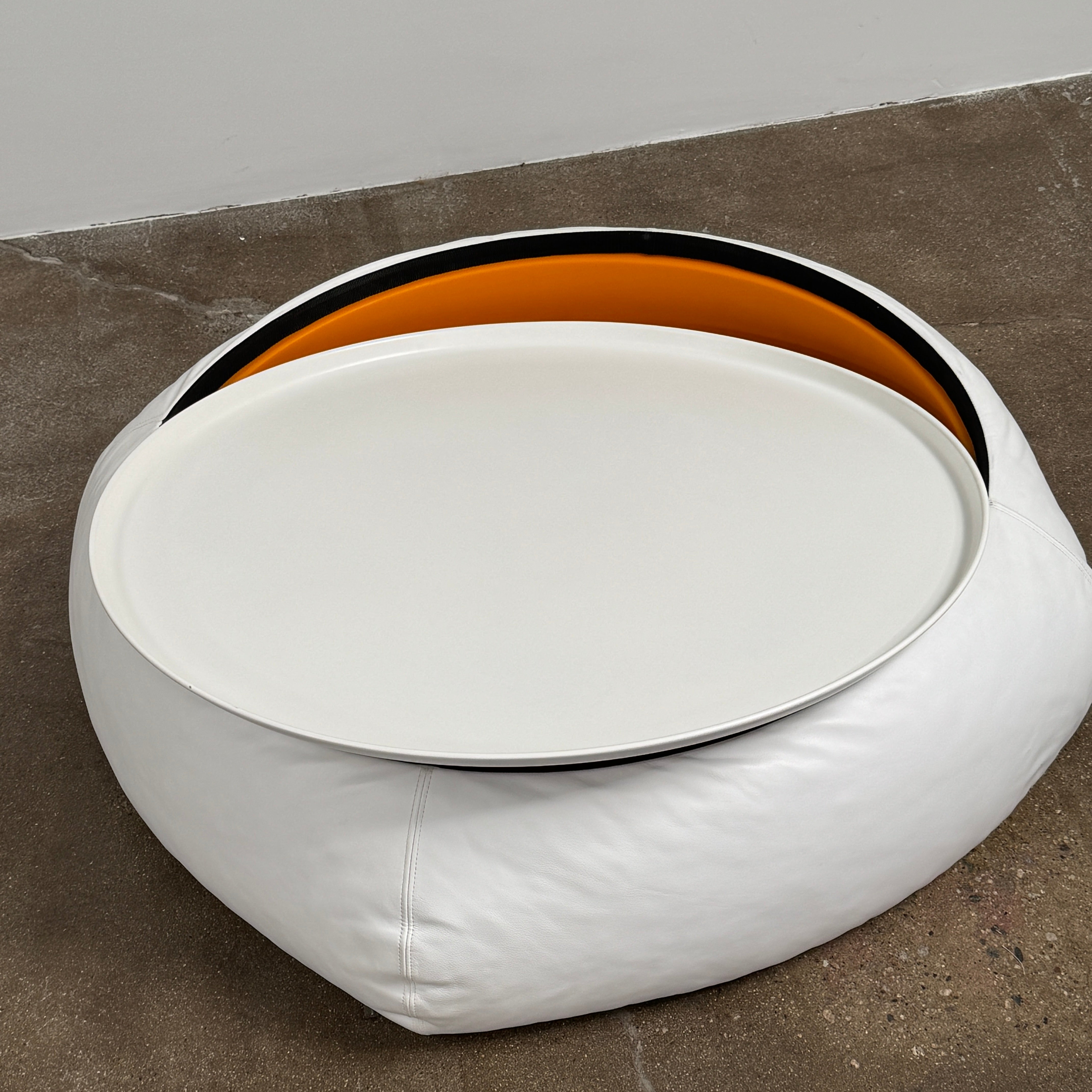 The B&B Italia Lady Fat Coffee Table by B&B Italia, a low, round table with a flat white top inspired by Patricia Urquiola’s design, sits on a plain brown floor against a light gray wall.