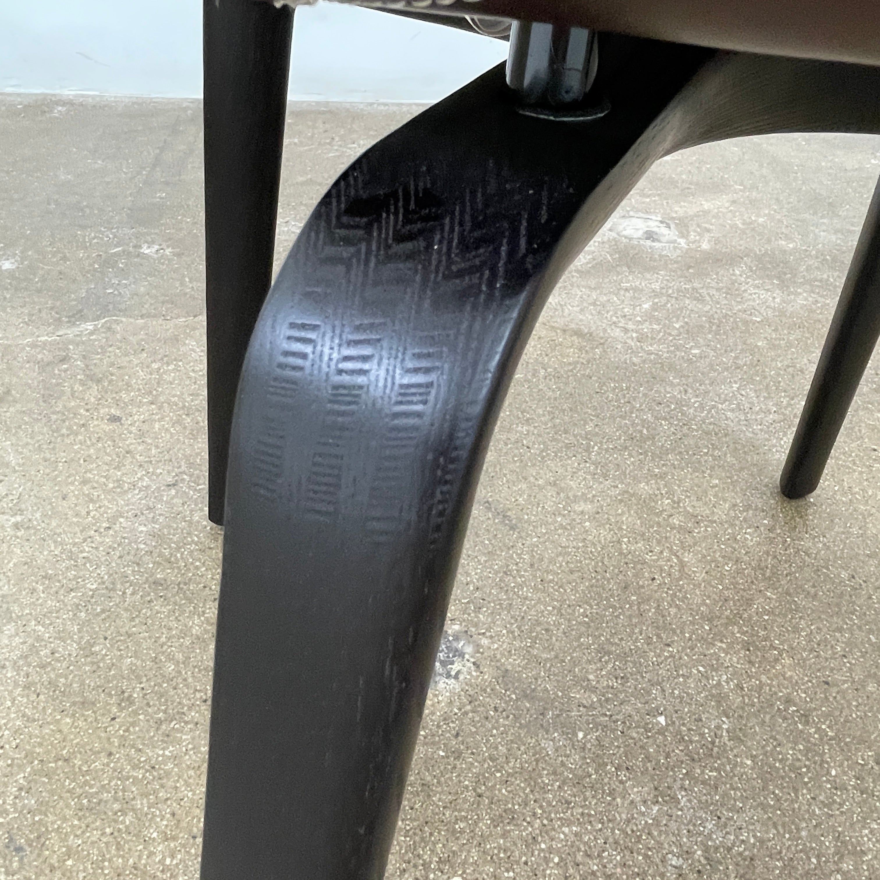 The Poltrona Frau Montera Small Blue Armchair, featuring a unique curved backrest and black legs, stands elegantly against a plain background.