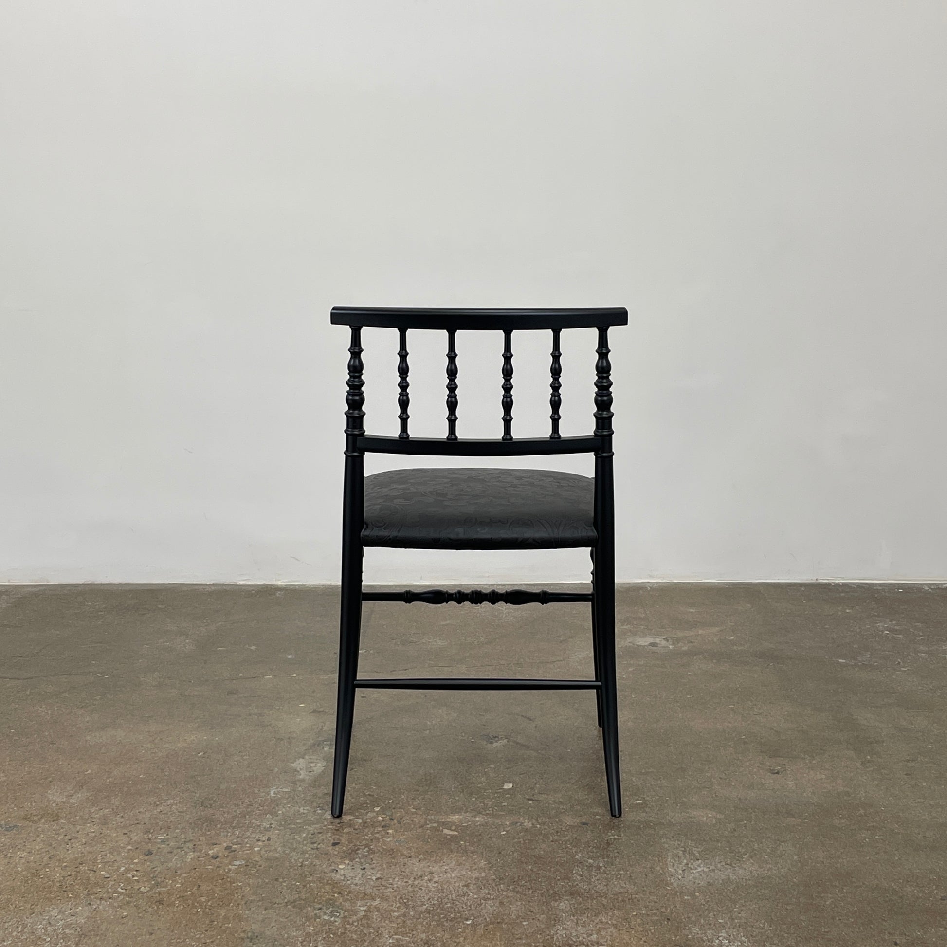 The Cappellini New Antiques Spindle Chair by Marcel Wanders for Cassina, in black wood, showcases a sleek backrest and cushioned seat when viewed from the front.