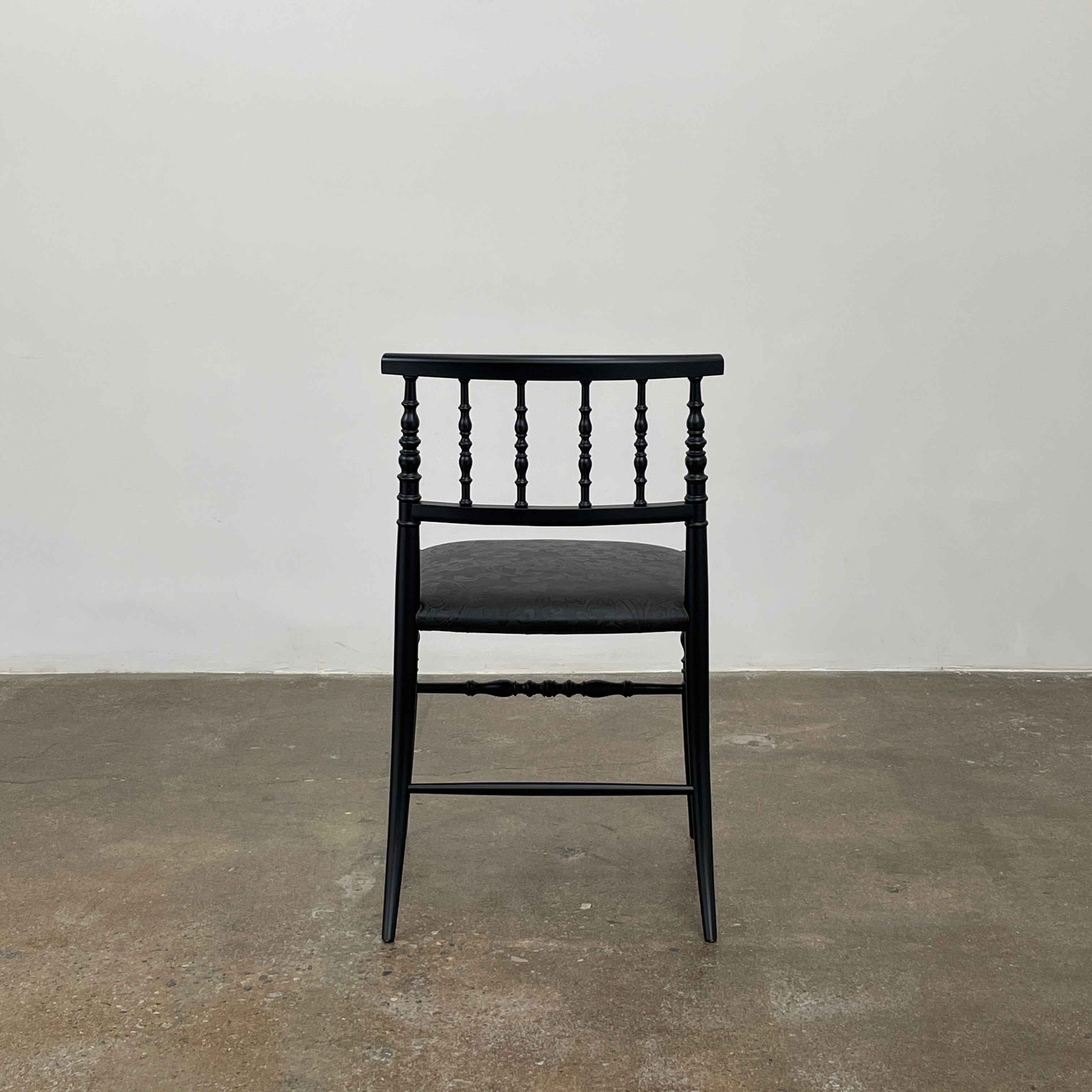 The Cappellini New Antiques Spindle Chair by Marcel Wanders for Cassina, in black wood, showcases a sleek backrest and cushioned seat when viewed from the front.