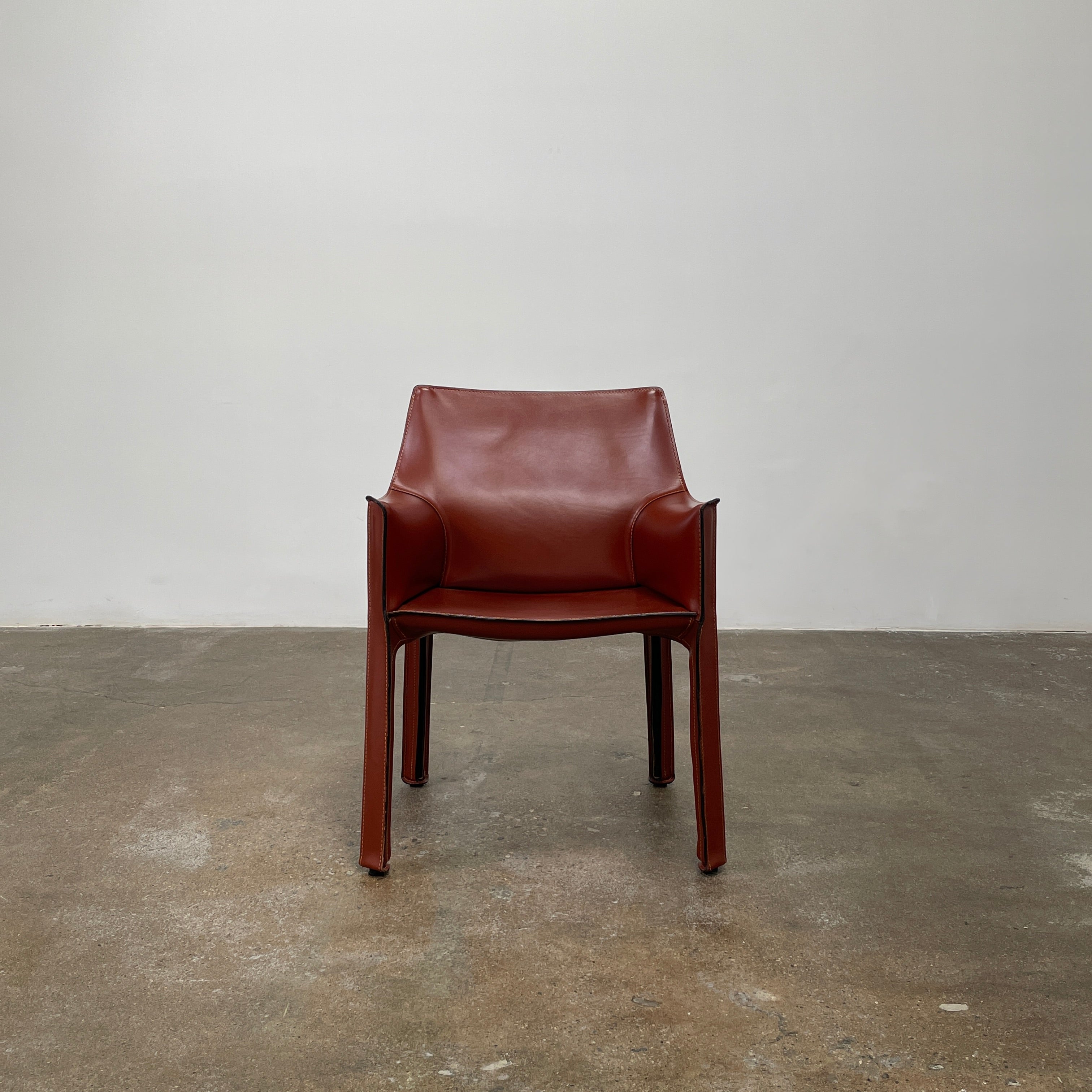 A red leather armchair, the Cassina Cab 413, drawing inspiration from the iconic Cab Chair with clean lines and a minimalist design, set against a plain grey background.