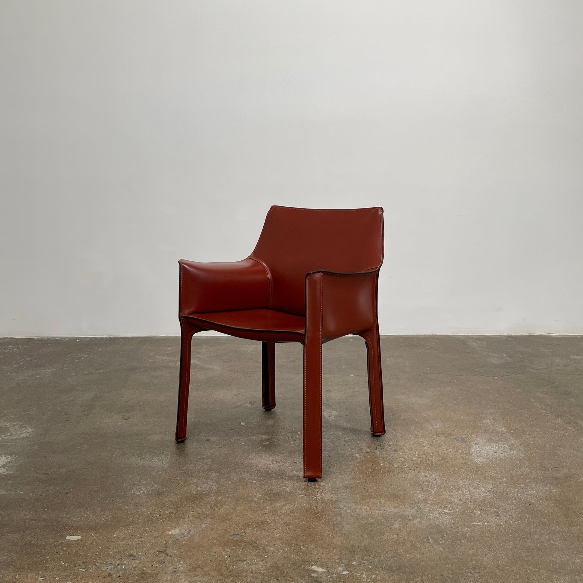 A red leather armchair, the Cassina Cab 413, drawing inspiration from the iconic Cab Chair with clean lines and a minimalist design, set against a plain grey background.