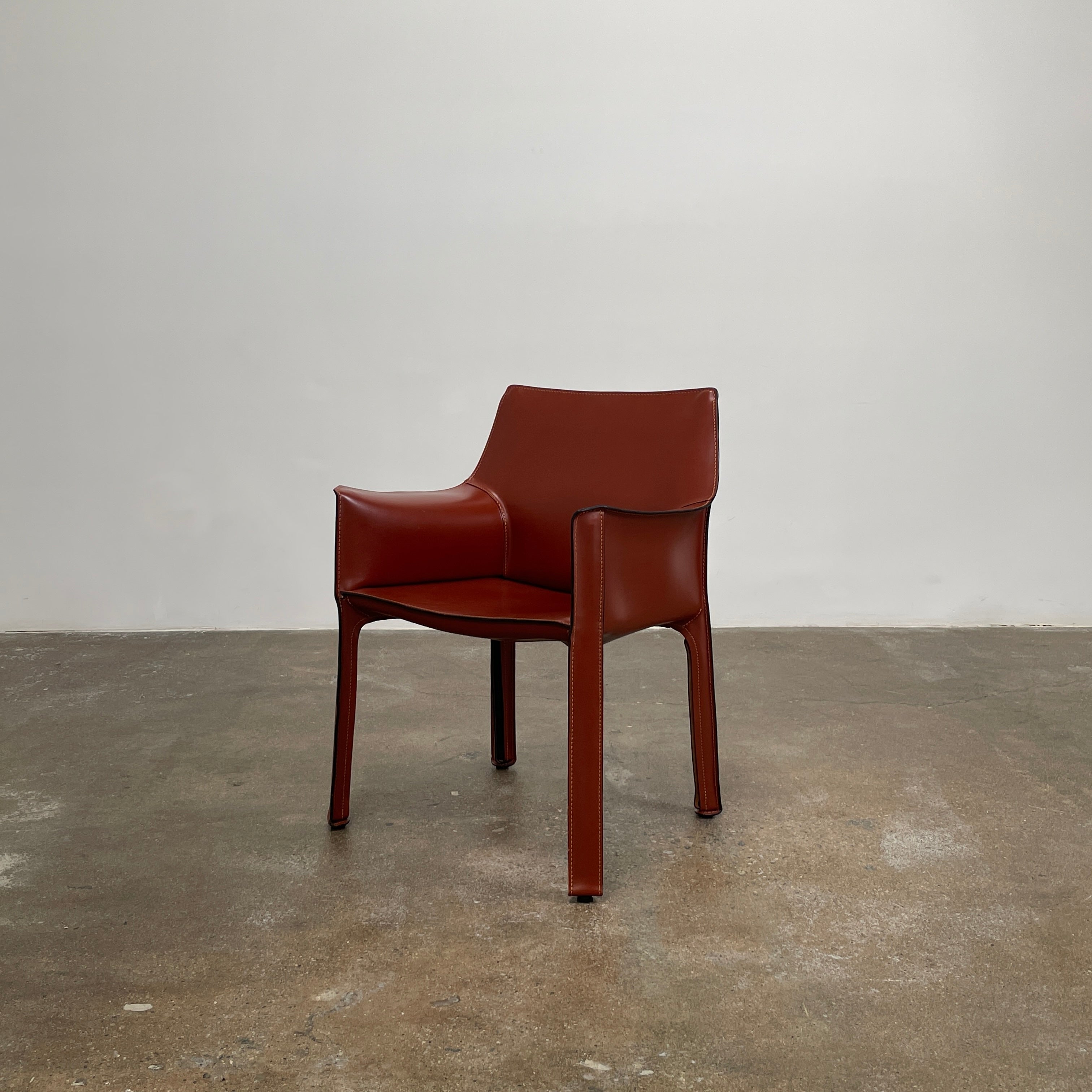 A red leather armchair, the Cassina Cab 413, drawing inspiration from the iconic Cab Chair with clean lines and a minimalist design, set against a plain grey background.