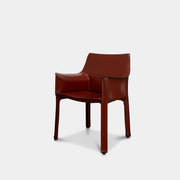 A red leather armchair, the Cassina Cab 413, drawing inspiration from the iconic Cab Chair with clean lines and a minimalist design, set against a plain grey background.