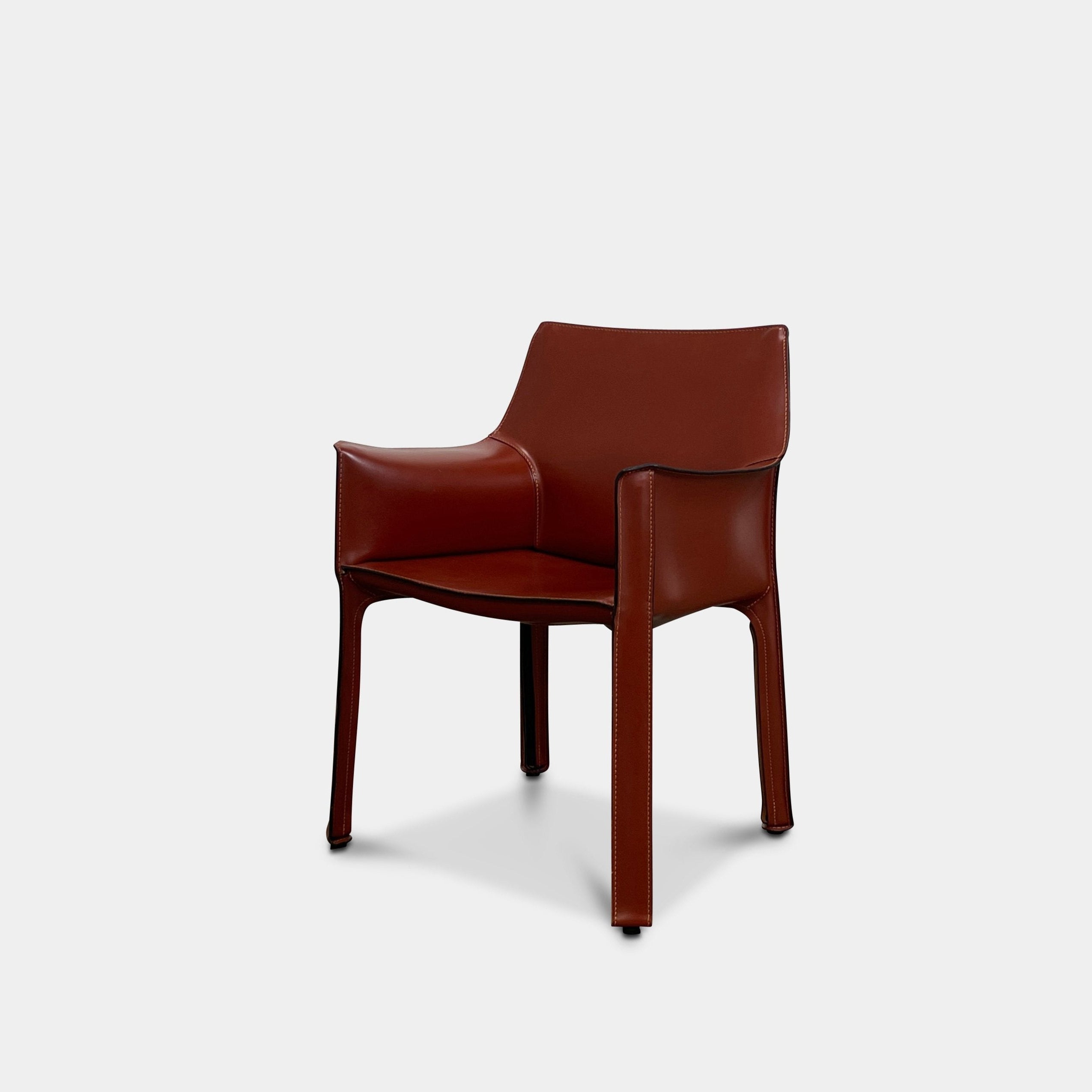 A red leather armchair, the Cassina Cab 413, drawing inspiration from the iconic Cab Chair with clean lines and a minimalist design, set against a plain grey background.
