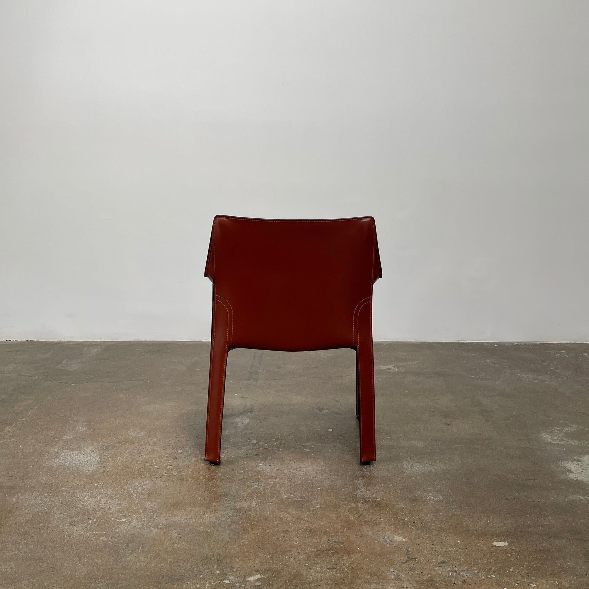 A red leather armchair, the Cassina Cab 413, drawing inspiration from the iconic Cab Chair with clean lines and a minimalist design, set against a plain grey background.