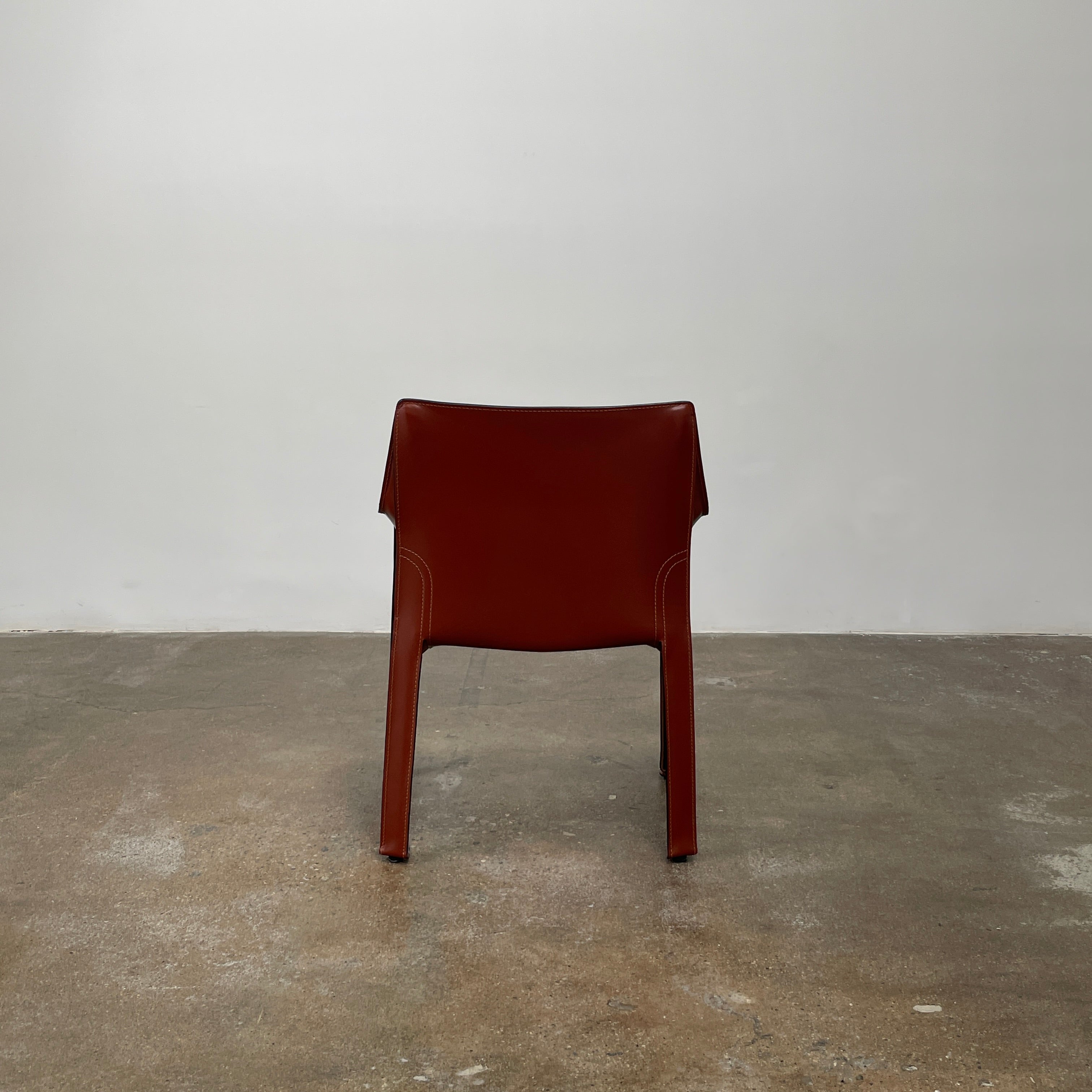 A red leather armchair, the Cassina Cab 413, drawing inspiration from the iconic Cab Chair with clean lines and a minimalist design, set against a plain grey background.