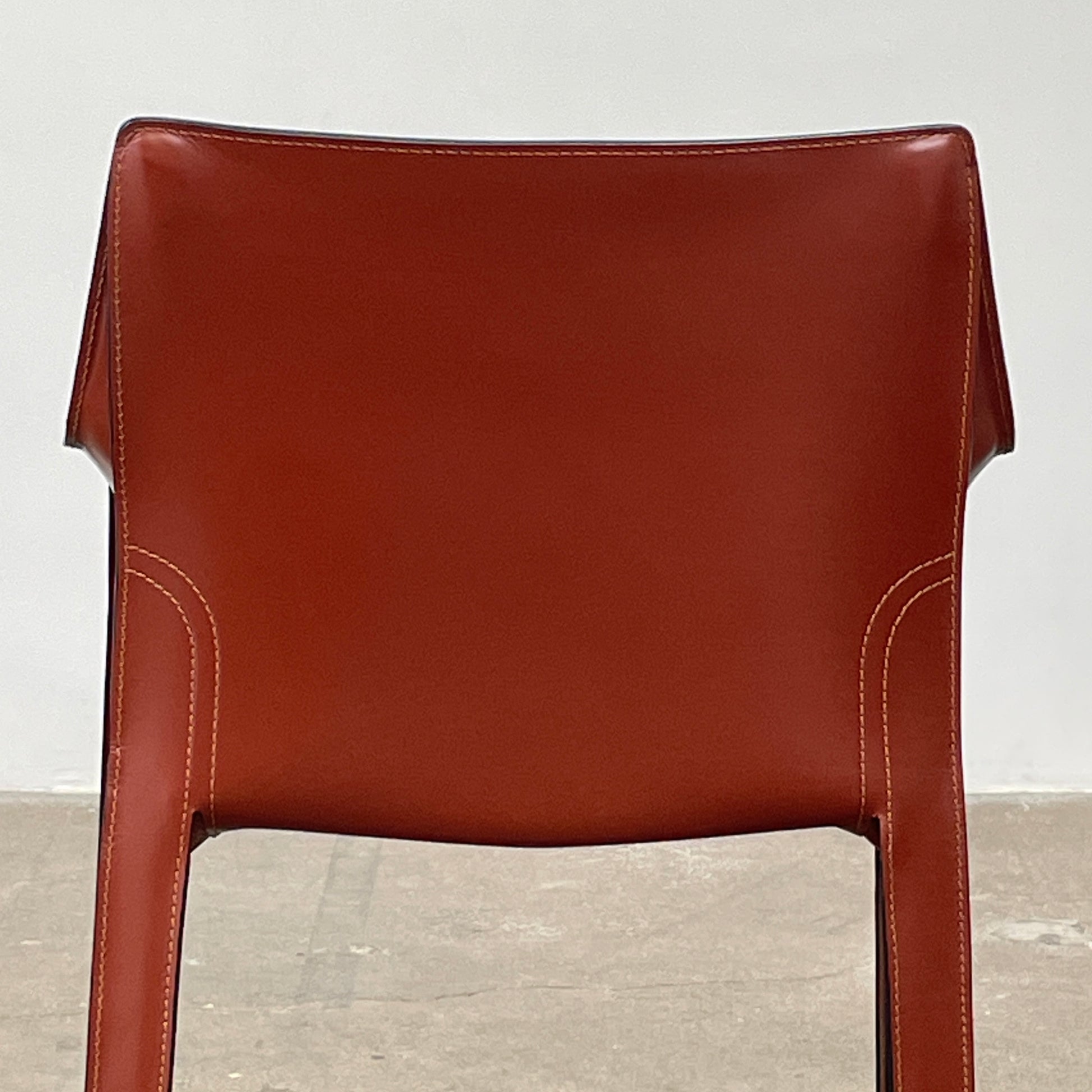 A red leather armchair, the Cassina Cab 413, drawing inspiration from the iconic Cab Chair with clean lines and a minimalist design, set against a plain grey background.