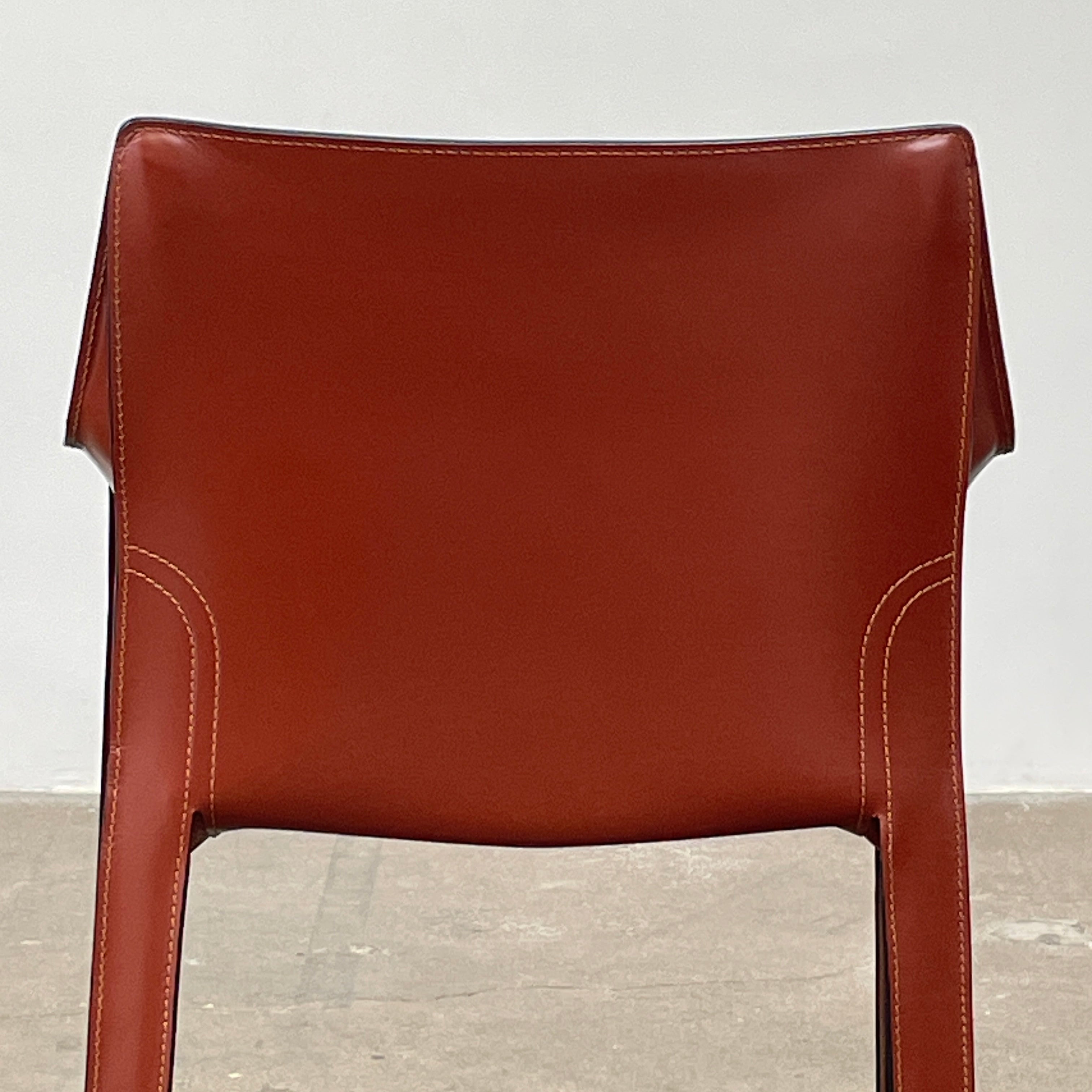 A red leather armchair, the Cassina Cab 413, drawing inspiration from the iconic Cab Chair with clean lines and a minimalist design, set against a plain grey background.