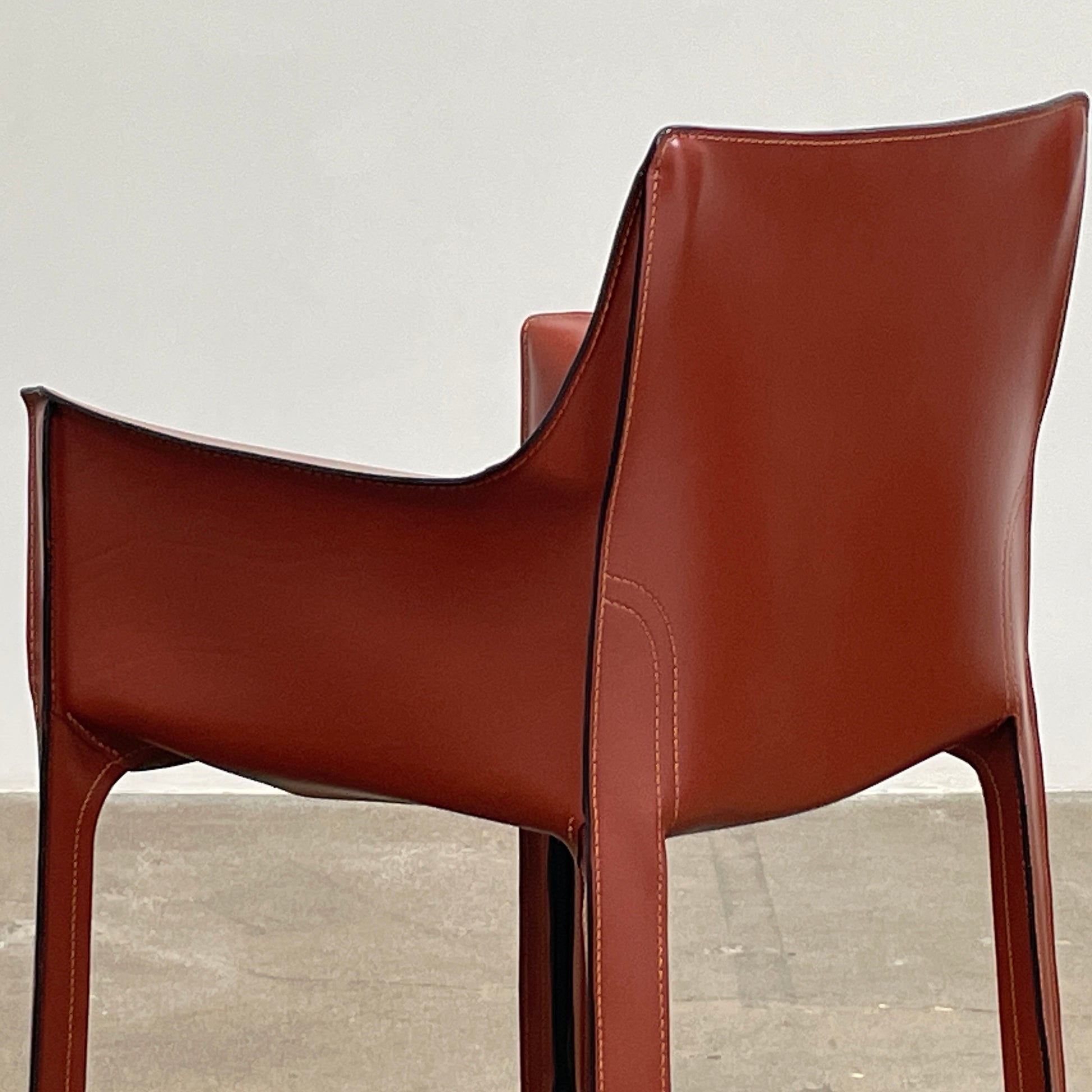 A red leather armchair, the Cassina Cab 413, drawing inspiration from the iconic Cab Chair with clean lines and a minimalist design, set against a plain grey background.