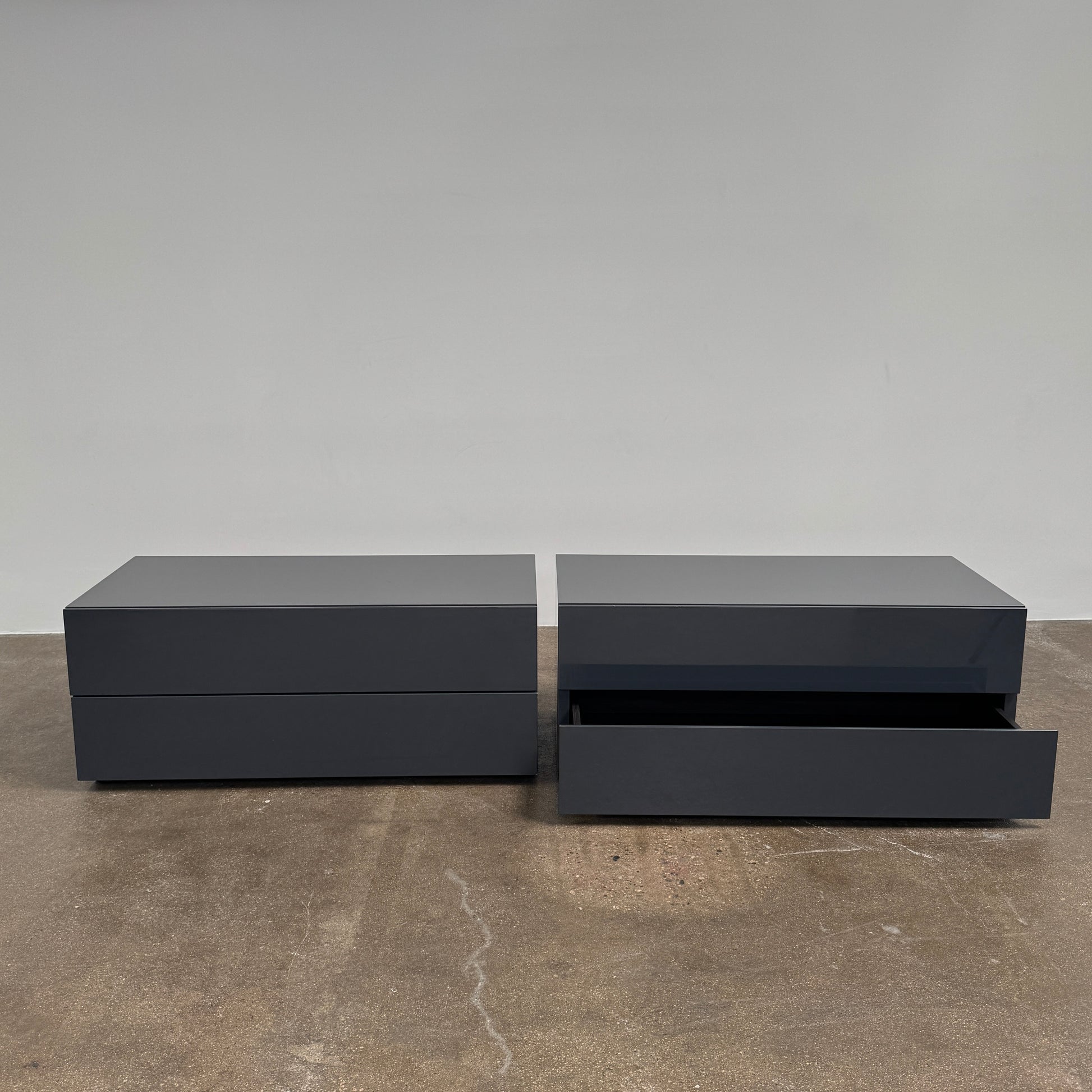 A pair of Poliform Dream Night Stands, each dark and rectangular with three drawers, stand side by side on a concrete floor against a plain white wall.