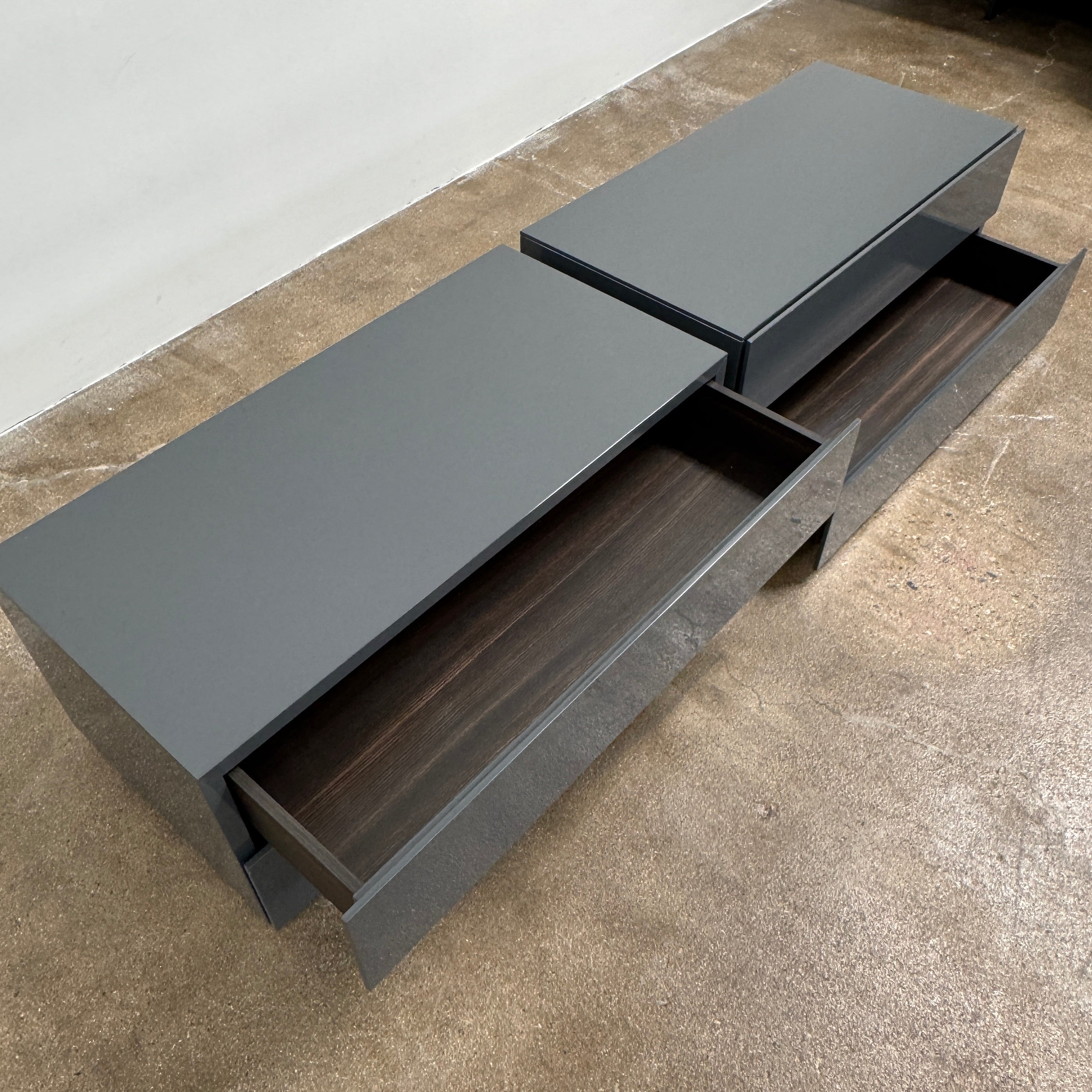 A pair of Poliform Dream Night Stands, each dark and rectangular with three drawers, stand side by side on a concrete floor against a plain white wall.