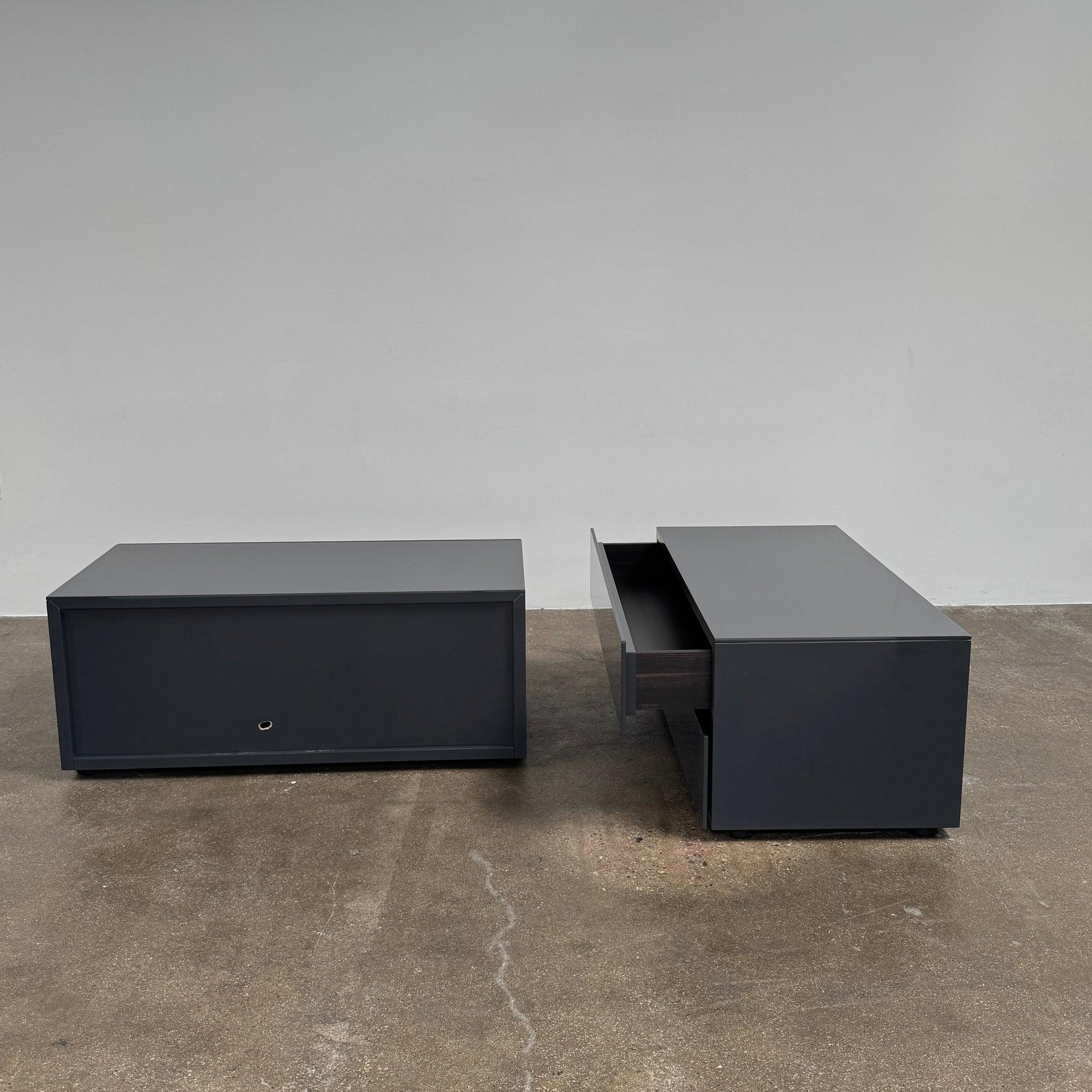 A pair of Poliform Dream Night Stands, each dark and rectangular with three drawers, stand side by side on a concrete floor against a plain white wall.