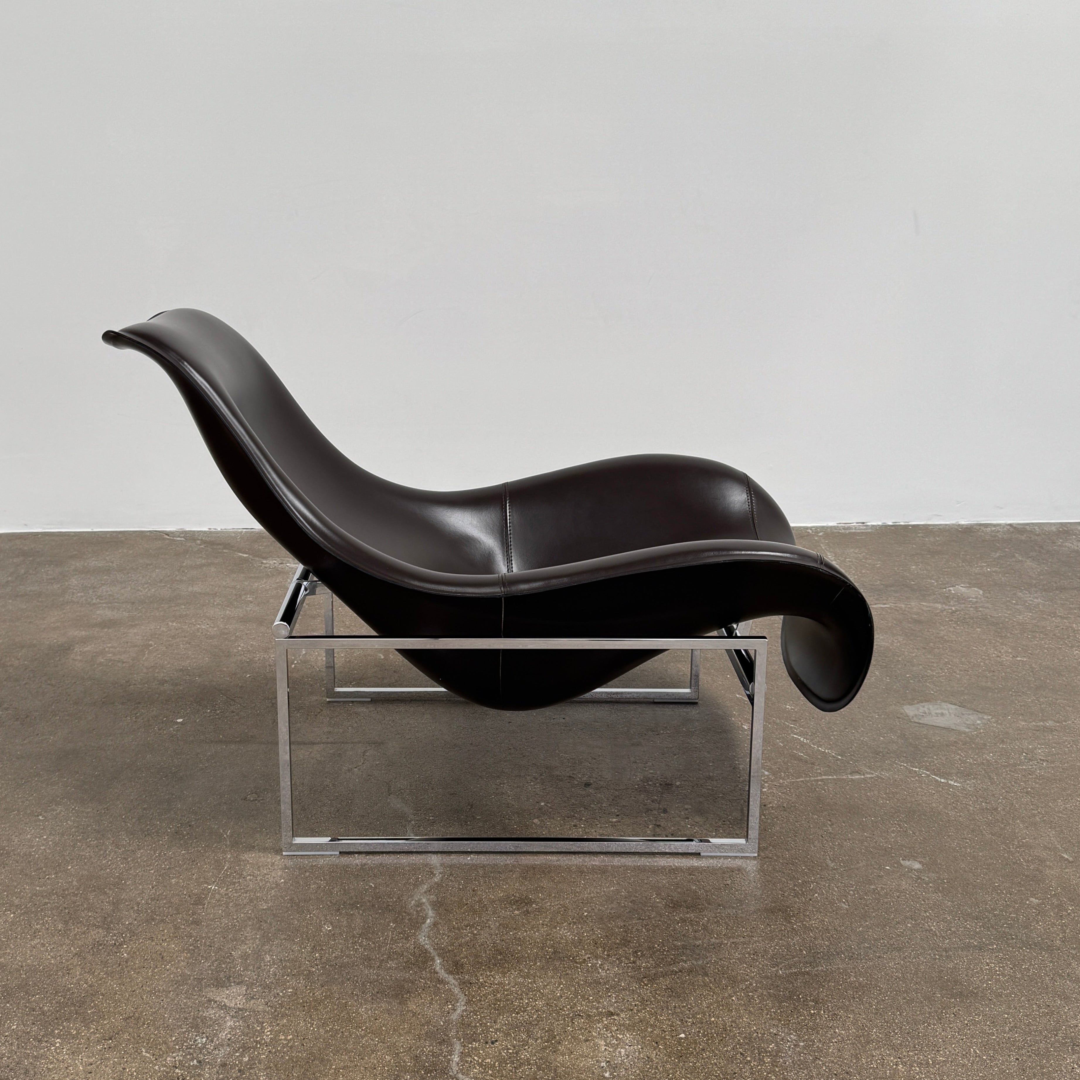 A B&B Italia Mart Relax Armchair with Tilting Mechanism in black saddle leather features a modern, curved design and is set on a polished concrete floor against a plain light gray wall.