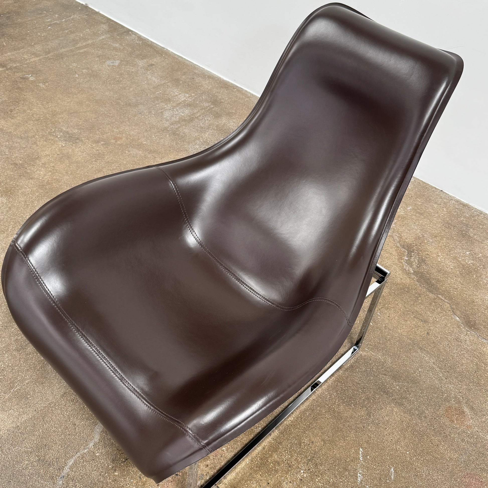 A B&B Italia Mart Relax Armchair with Tilting Mechanism in black saddle leather features a modern, curved design and is set on a polished concrete floor against a plain light gray wall.