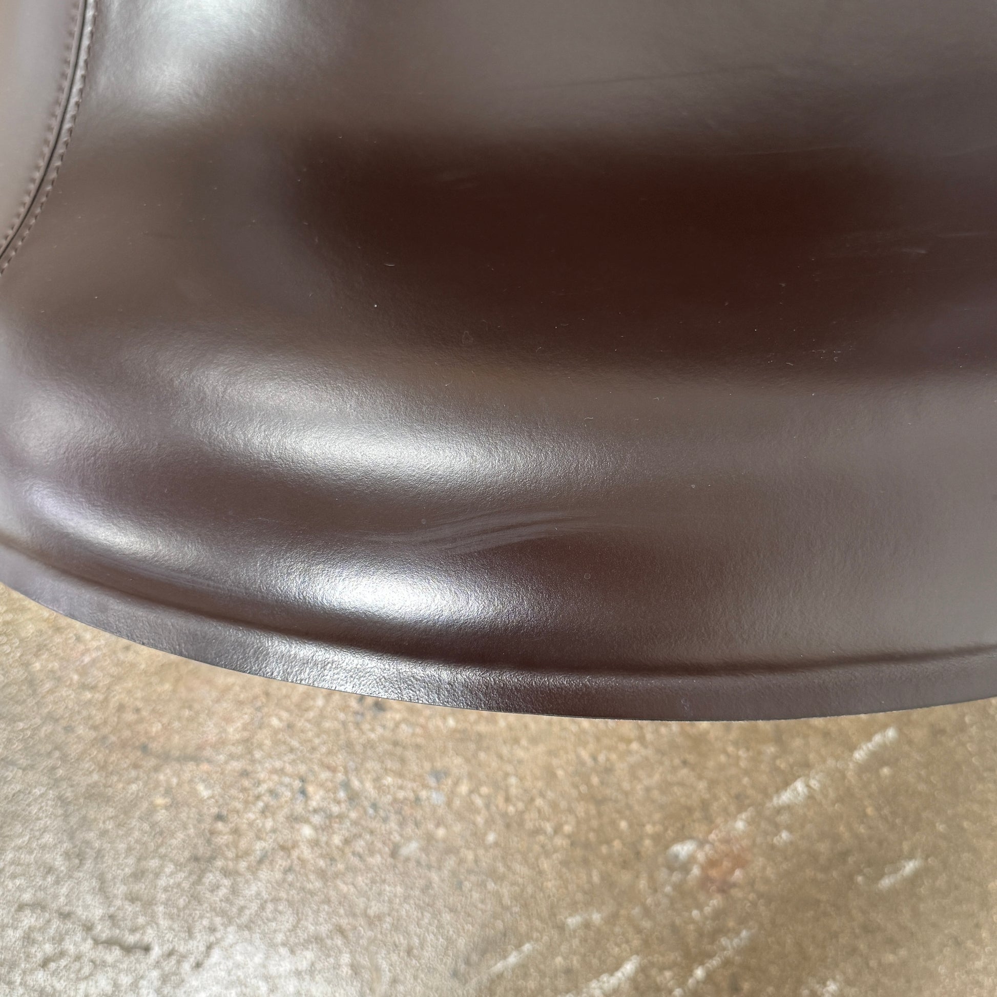 A B&B Italia Mart Relax Armchair with Tilting Mechanism in black saddle leather features a modern, curved design and is set on a polished concrete floor against a plain light gray wall.