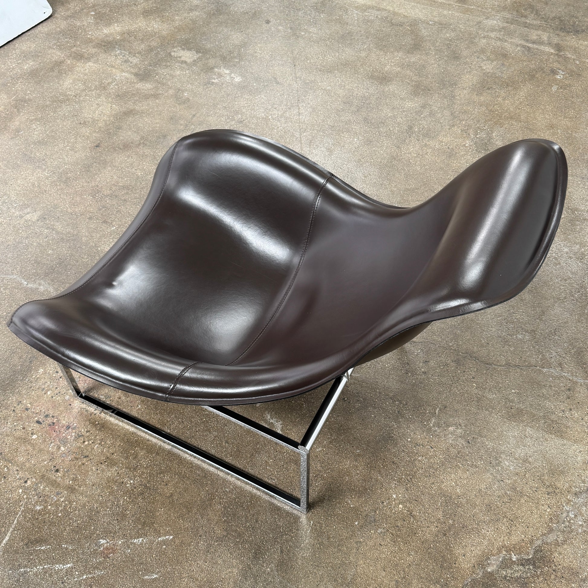 A B&B Italia Mart Relax Armchair with Tilting Mechanism in black saddle leather features a modern, curved design and is set on a polished concrete floor against a plain light gray wall.