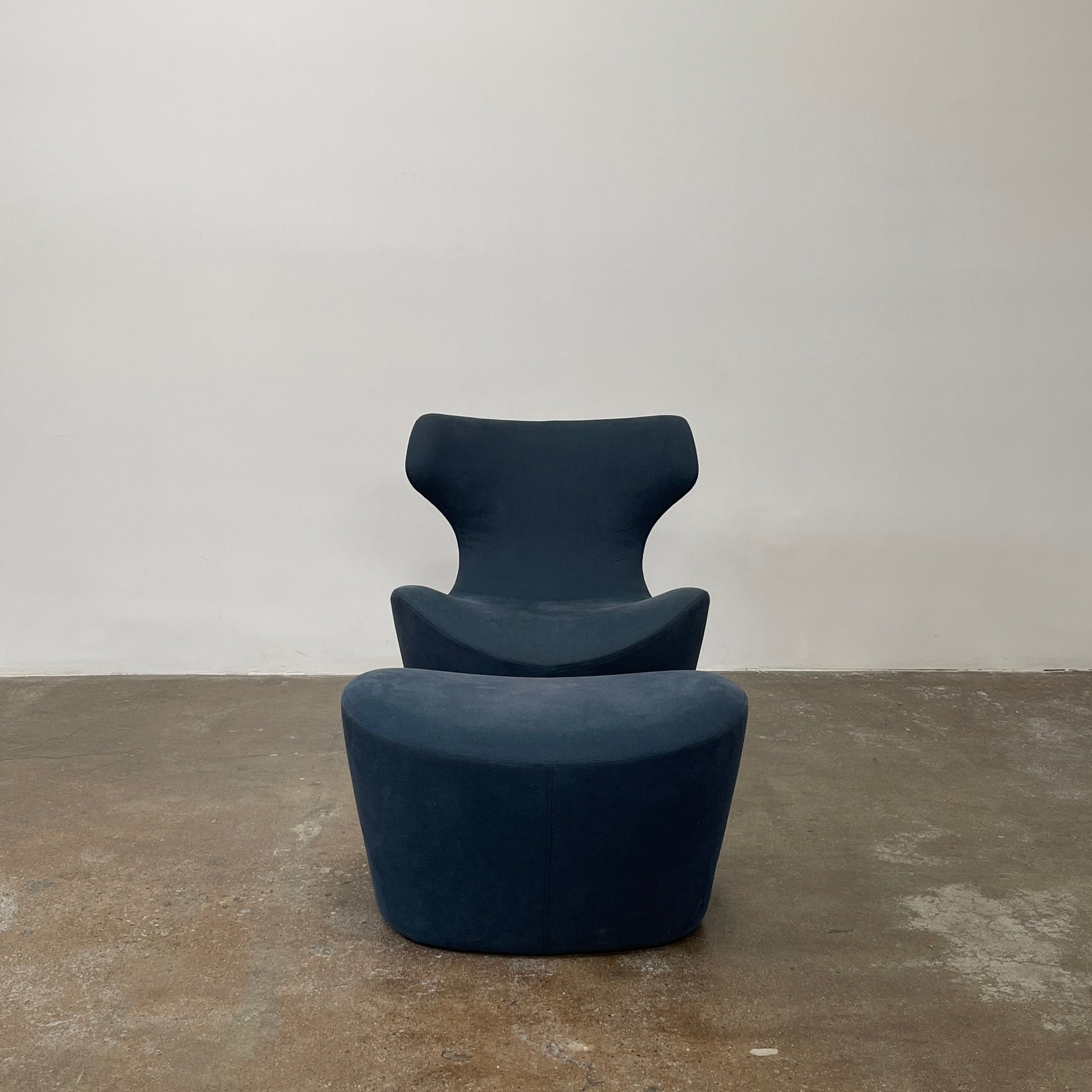 The B&B Italia Piccola Papilio Swivel Armchair is a modern piece with an abstract form and high curved backrest. Made from teal fabric, it stands on a swivel base against a plain white background.