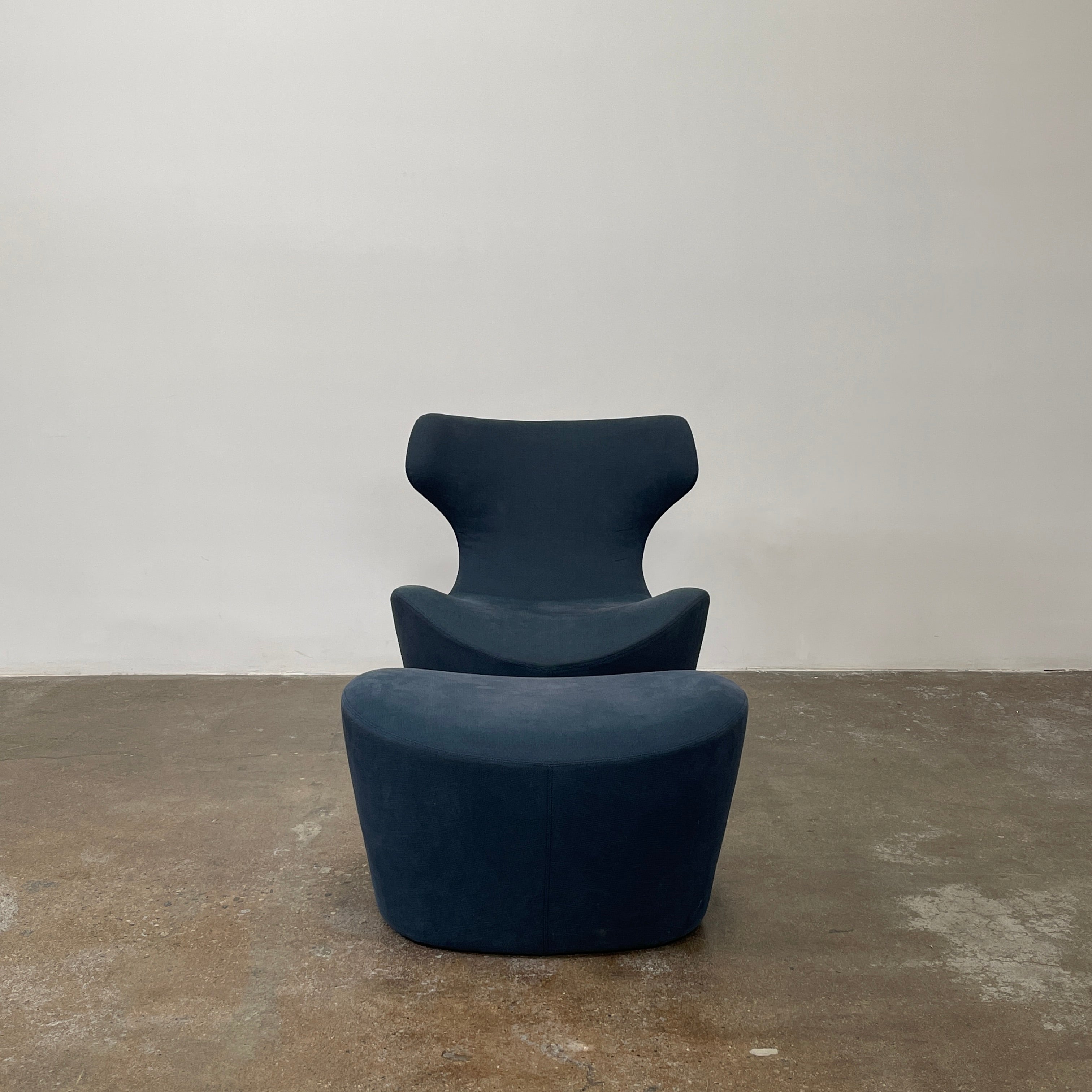 The B&B Italia Piccola Papilio Swivel Armchair is a modern piece with an abstract form and high curved backrest. Made from teal fabric, it stands on a swivel base against a plain white background.