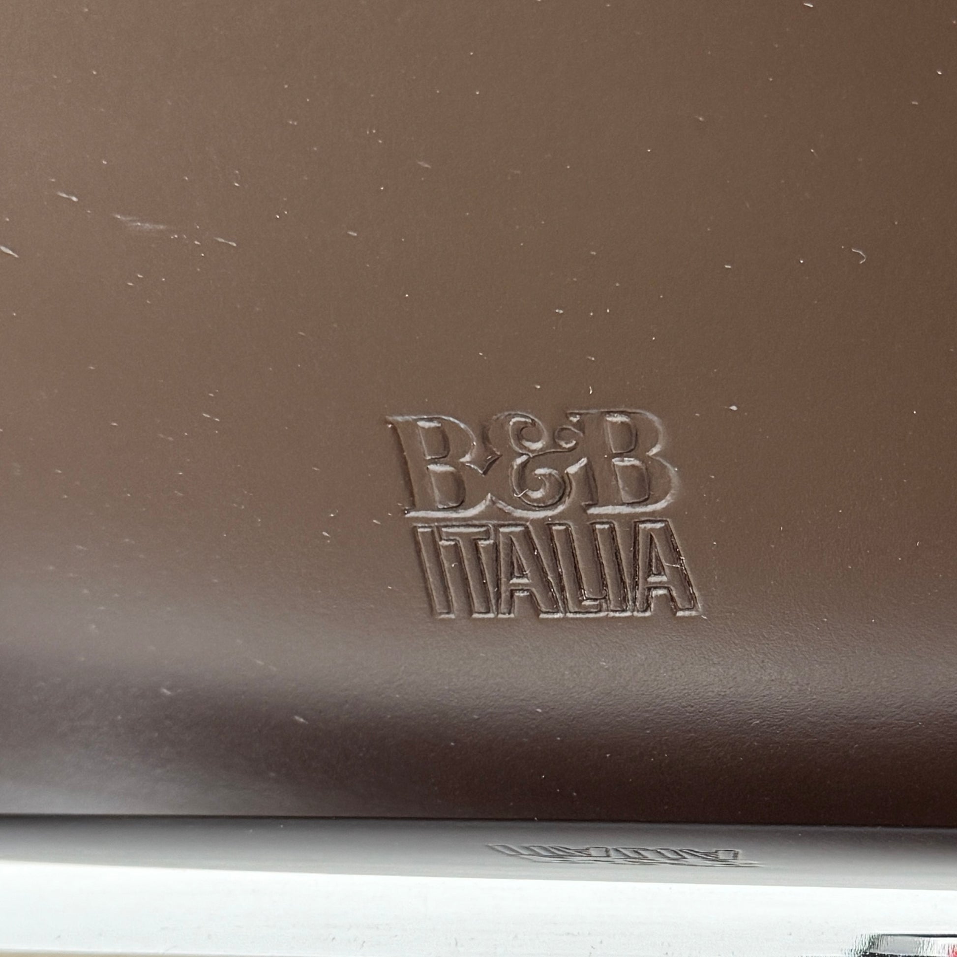 A B&B Italia Mart Relax Armchair with Tilting Mechanism in black saddle leather features a modern, curved design and is set on a polished concrete floor against a plain light gray wall.