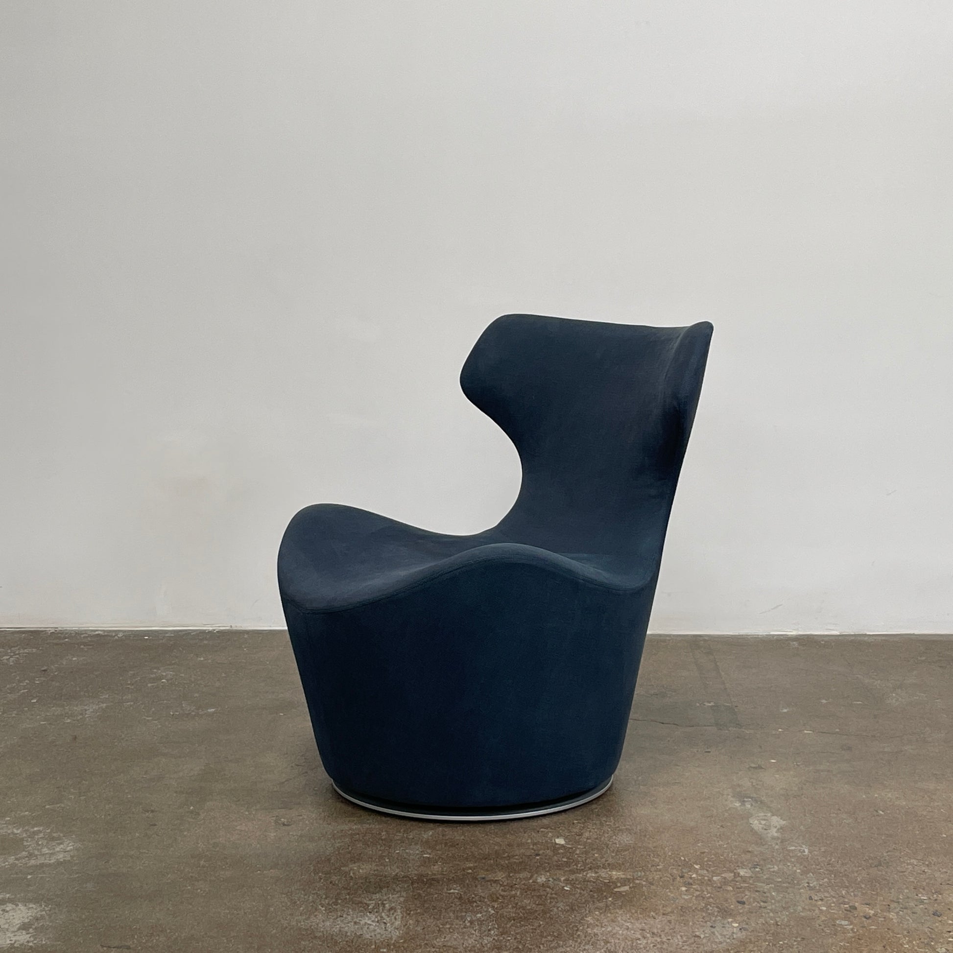 The B&B Italia Piccola Papilio Swivel Armchair is a modern piece with an abstract form and high curved backrest. Made from teal fabric, it stands on a swivel base against a plain white background.