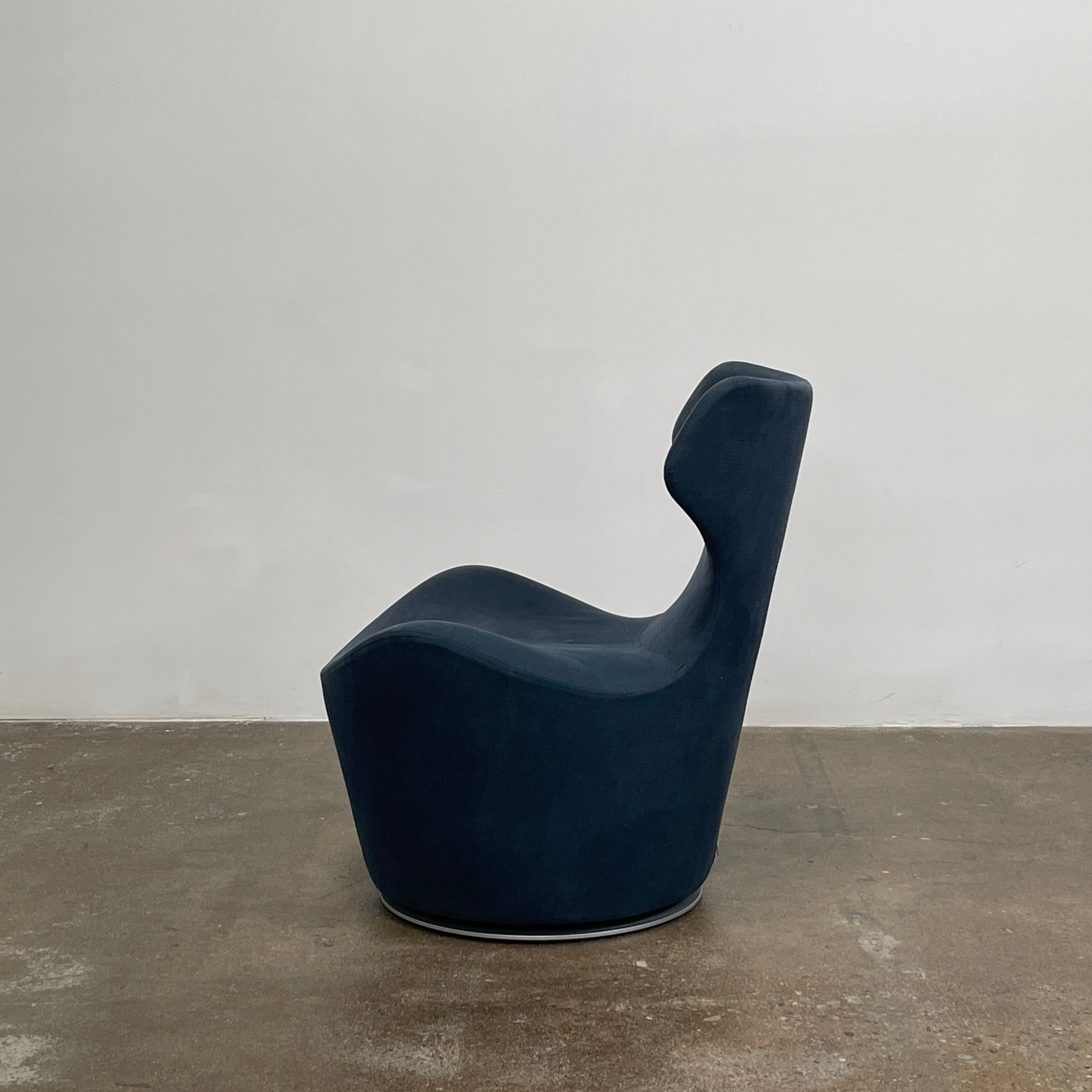 The B&B Italia Piccola Papilio Swivel Armchair is a modern piece with an abstract form and high curved backrest. Made from teal fabric, it stands on a swivel base against a plain white background.