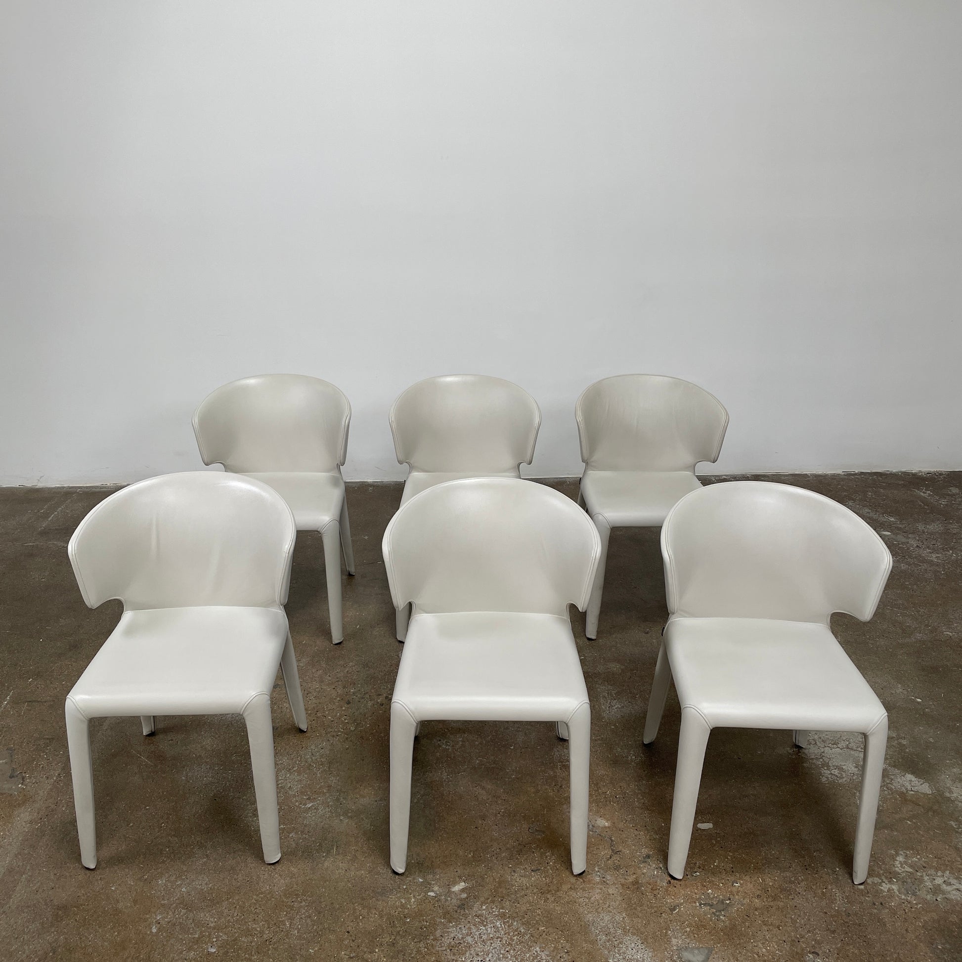 Six Cassina Hola 367 Dining Chairs, identical and upholstered in white leather, are elegantly arranged in two rows on a plain background.