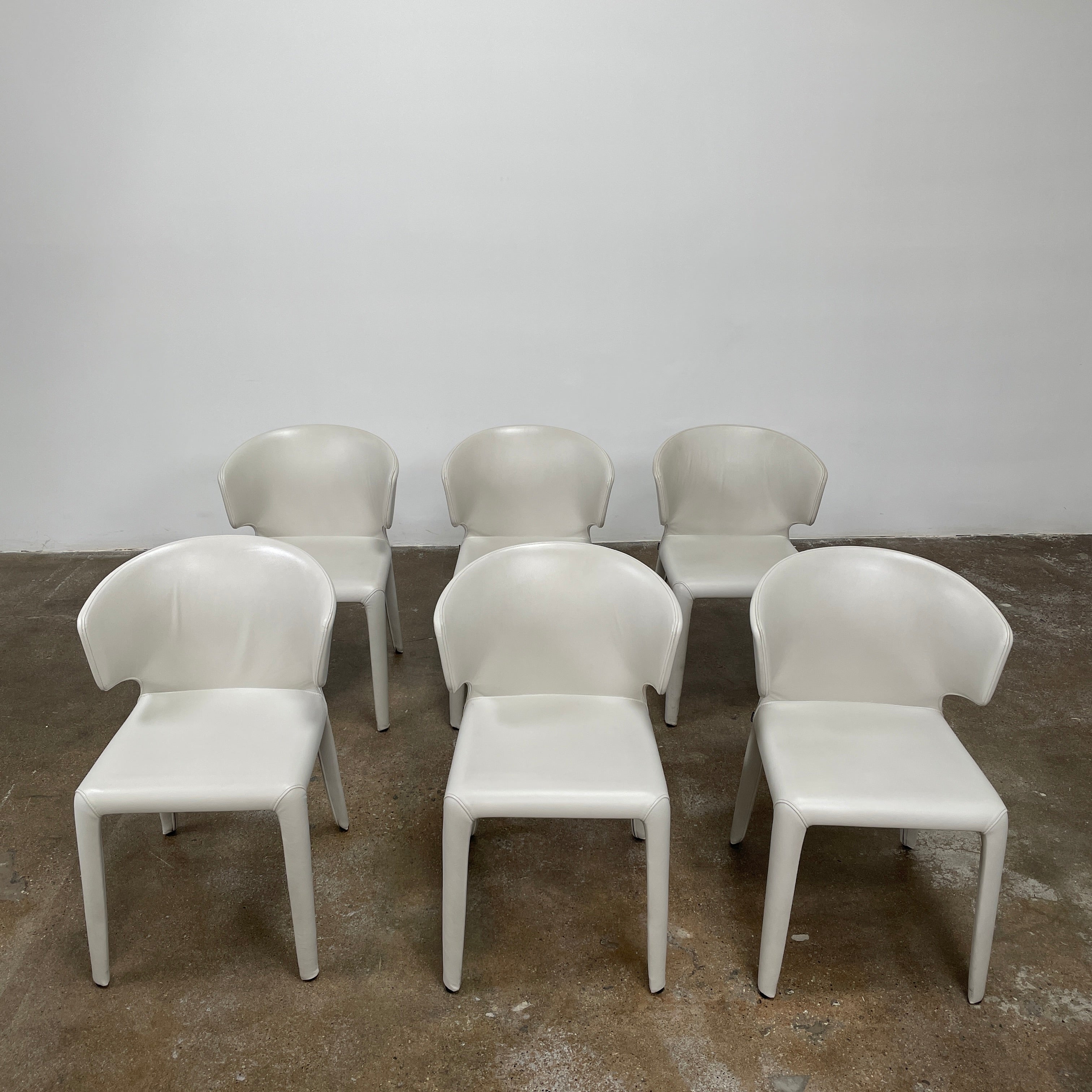 Six Cassina Hola 367 Dining Chairs, identical and upholstered in white leather, are elegantly arranged in two rows on a plain background.