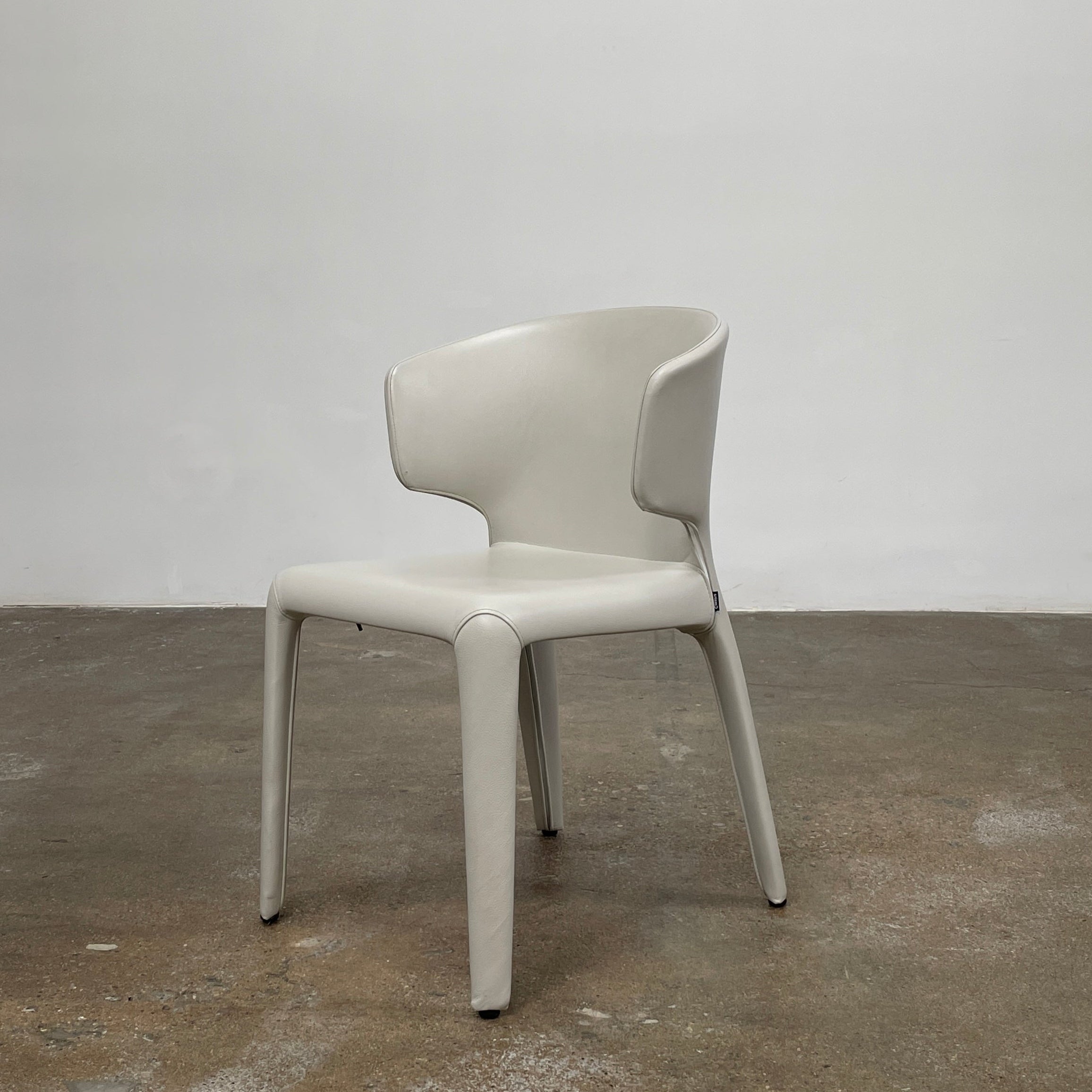 Six Cassina Hola 367 Dining Chairs, identical and upholstered in white leather, are elegantly arranged in two rows on a plain background.