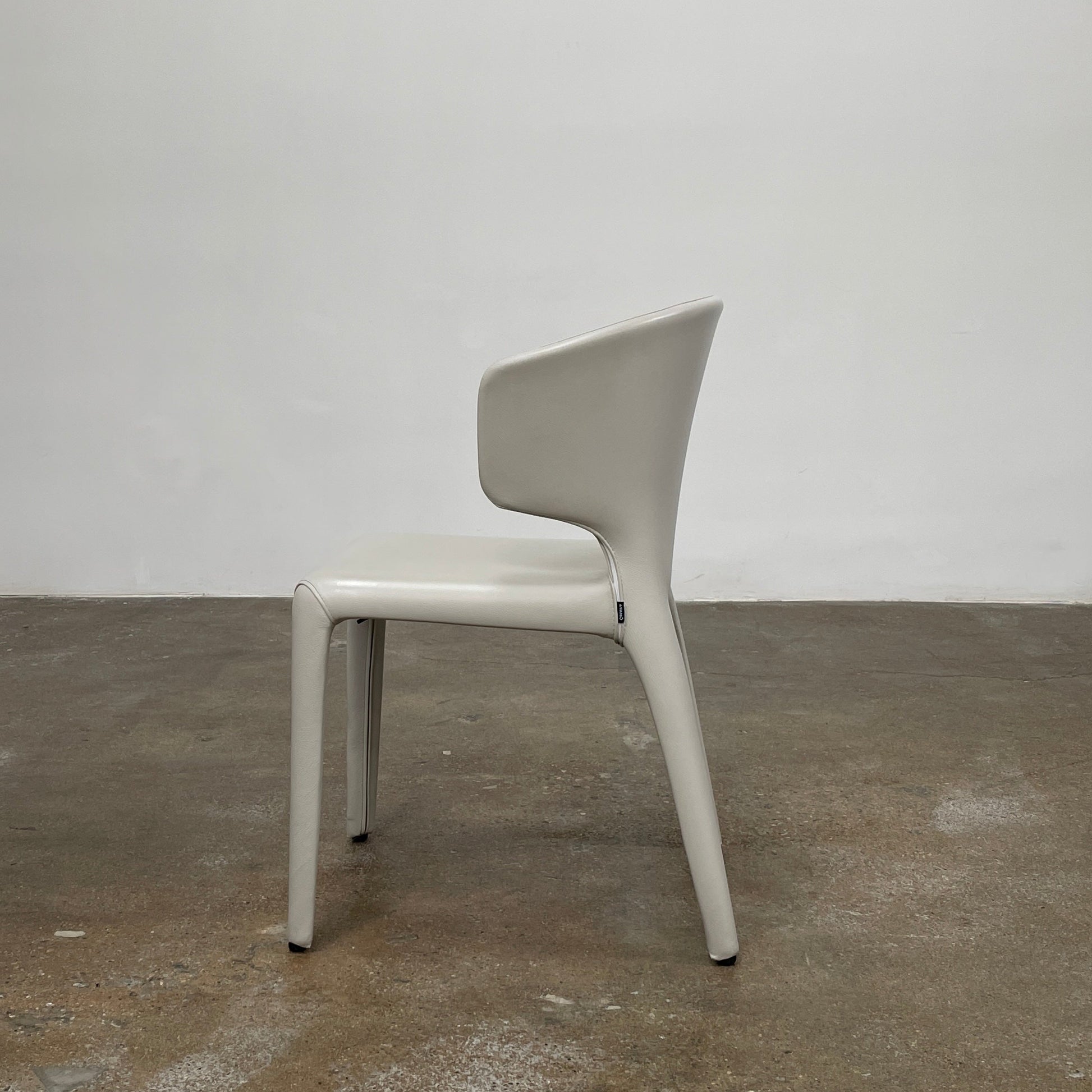 Six Cassina Hola 367 Dining Chairs, identical and upholstered in white leather, are elegantly arranged in two rows on a plain background.