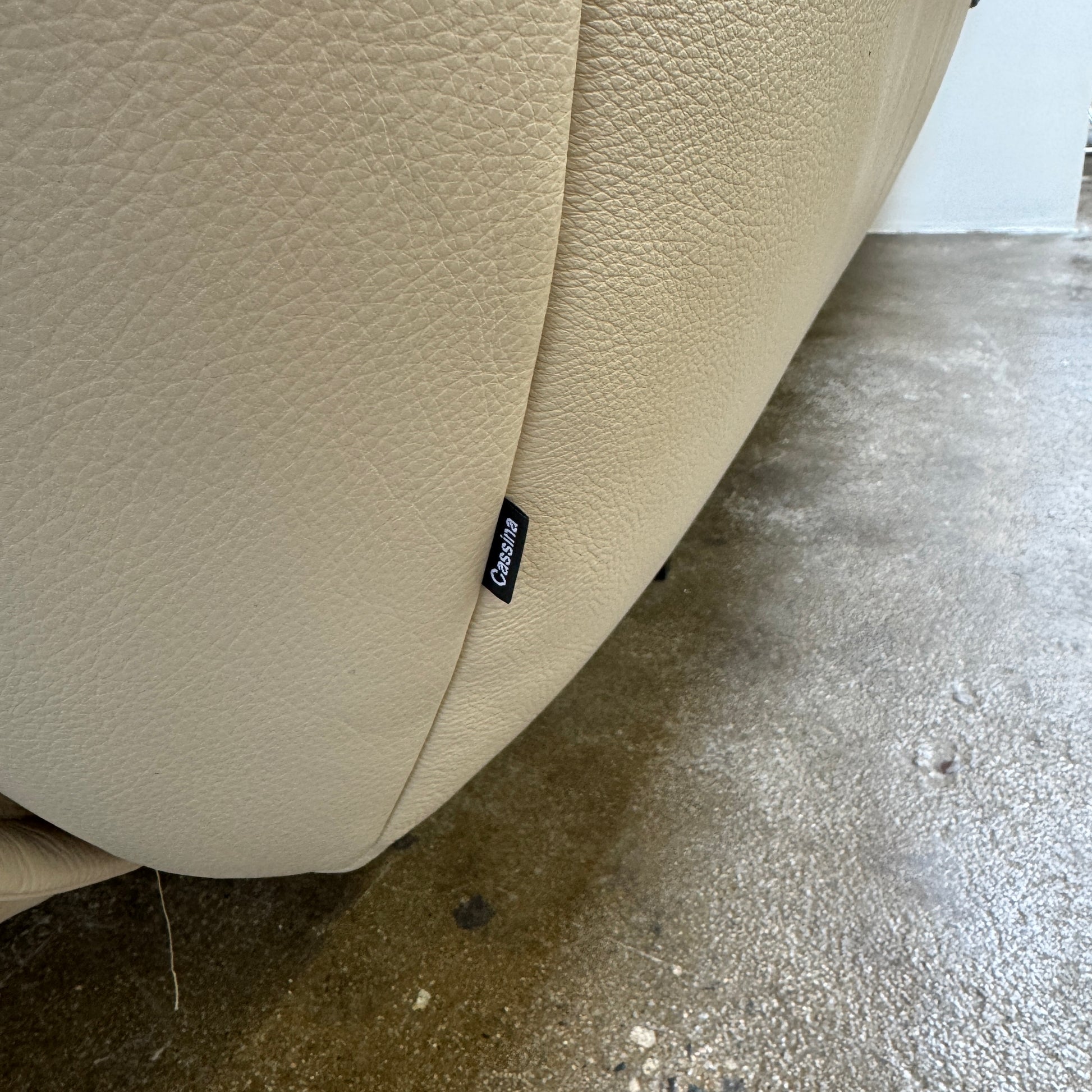 The Cassina Superbeam 5 Piece Leather Sectional in beige, featuring plush cushions, is arranged in a spacious room with white walls, exposed Superbeam ceiling, and overhead lighting.