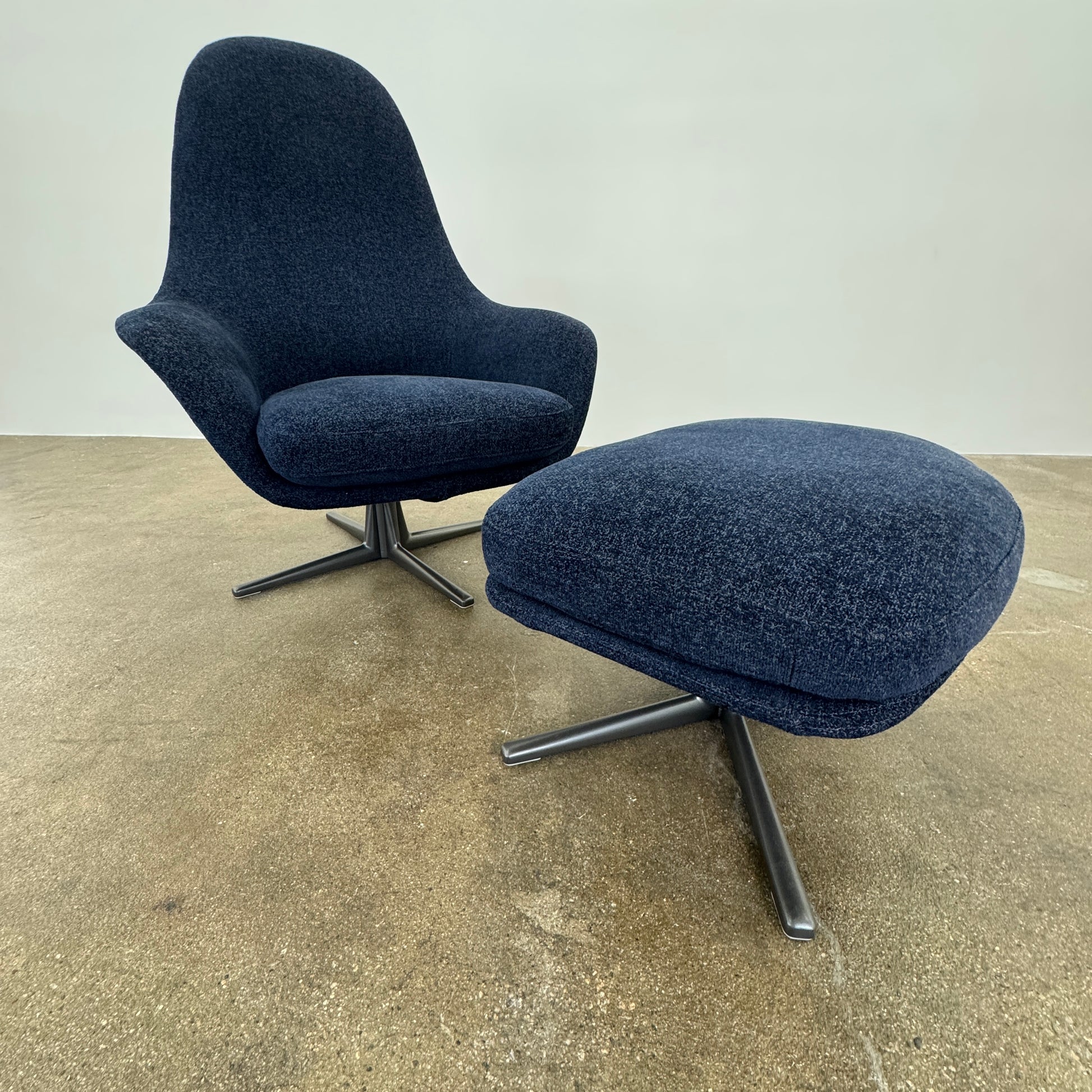 The Flexform Marlon Swivel Armchair and Ottoman, available with two covers, feature ergonomic design and black metal bases from Flexform, shown here in a modern gray finish against a plain white background.