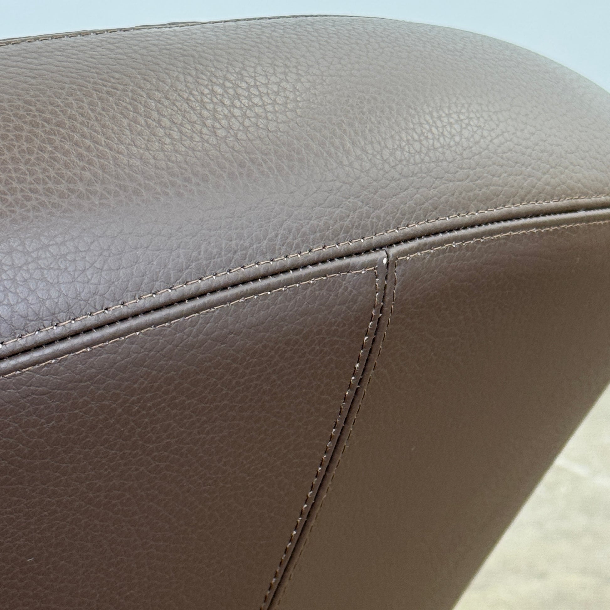 The Roche Bobois Nuage Swivel Chair is a modern, circular brown leather chair with a curved backrest and seat on a metal swivel base, set on a concrete floor against a plain white wall.