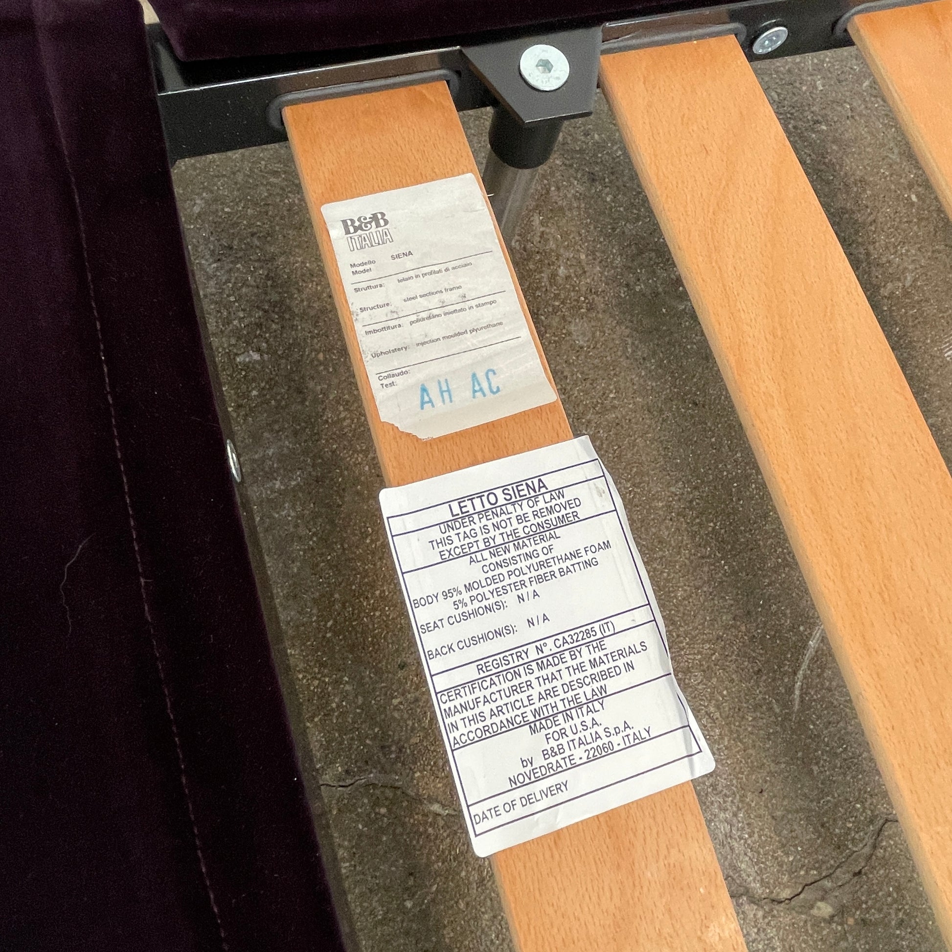 The B&B Italia Siena King Bed is a modern platform with wooden slats and an angled headboard, featuring a luxurious dark upholstered frame and sleek metal legs. Inspired by Naoto Fukasawa, it embodies understated elegance and sophistication for any contemporary bedroom setting.