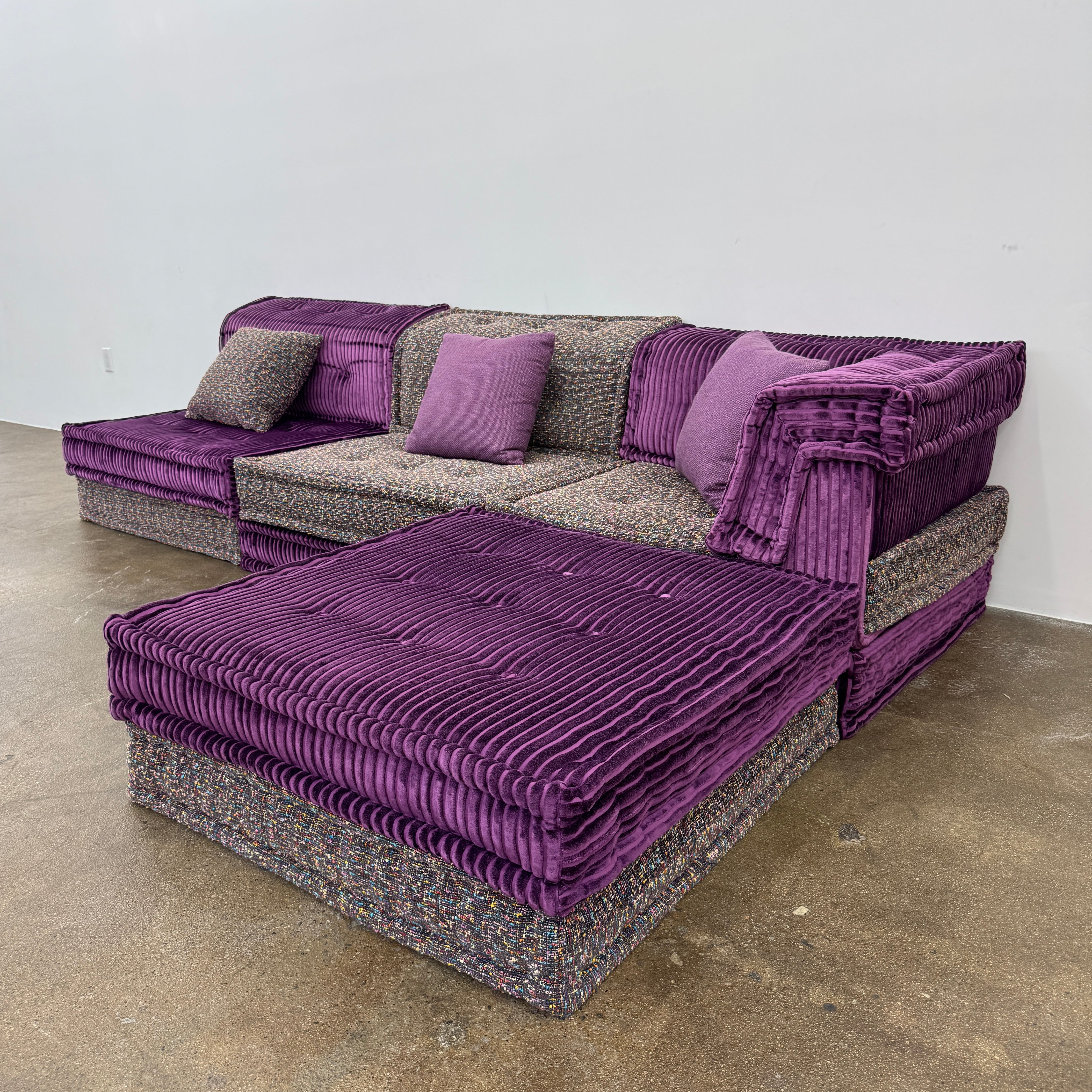 The Roche Bobois Mah Jong Sectional - Back with Mechanism by Roche Bobois features a modern modular design, purple and gray corduroy upholstery, and includes two purple throw pillows, inspired by the iconic Mah Jong sofa.