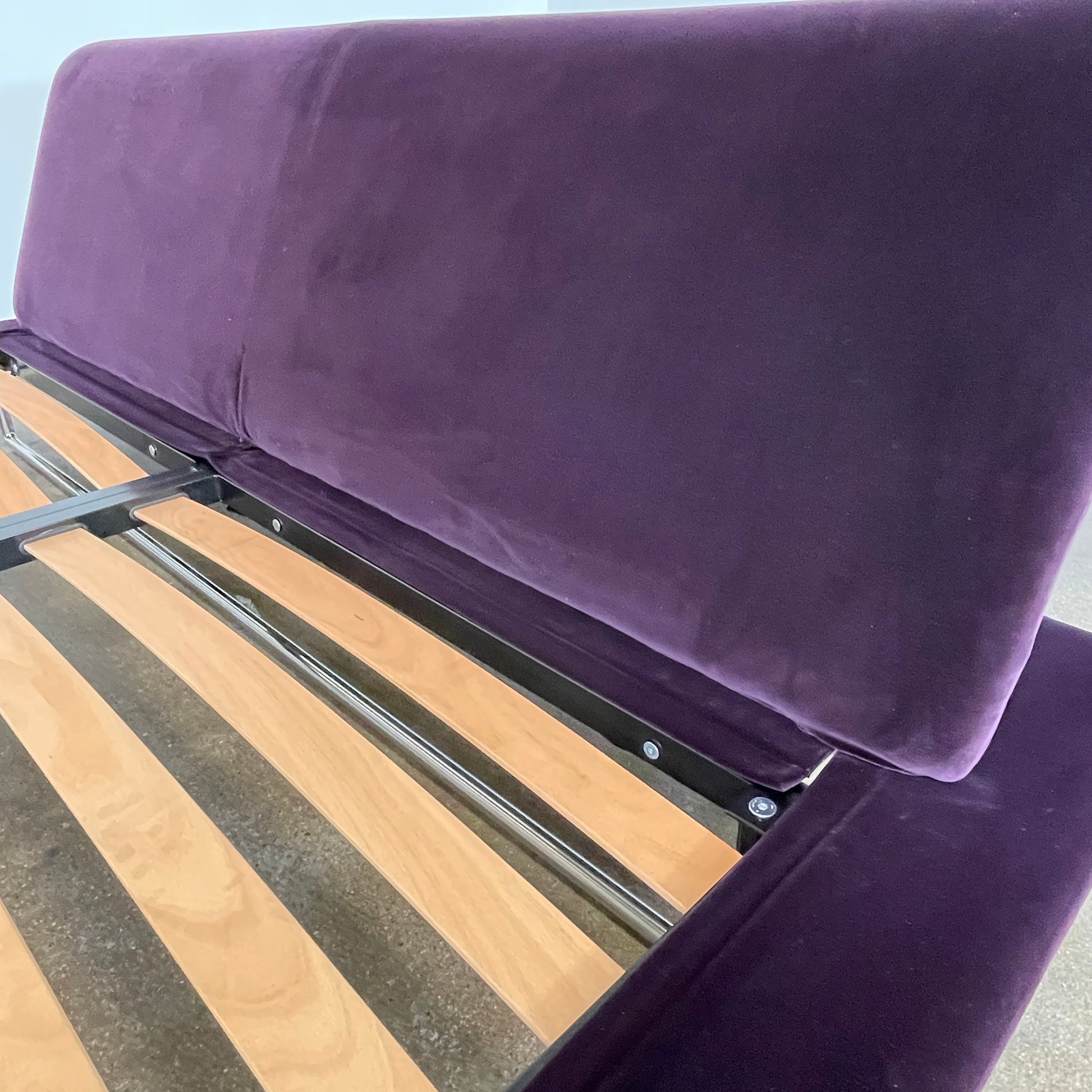 The B&B Italia Siena King Bed is a modern platform with wooden slats and an angled headboard, featuring a luxurious dark upholstered frame and sleek metal legs. Inspired by Naoto Fukasawa, it embodies understated elegance and sophistication for any contemporary bedroom setting.