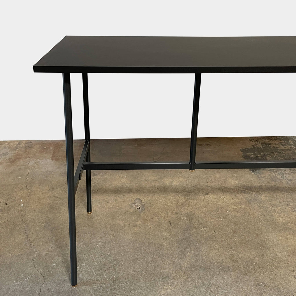 A black Normann Copenhagen Union Bar Table with a minimalist design and a metal frame, featuring shiny brass feet, set against a crisp white background.