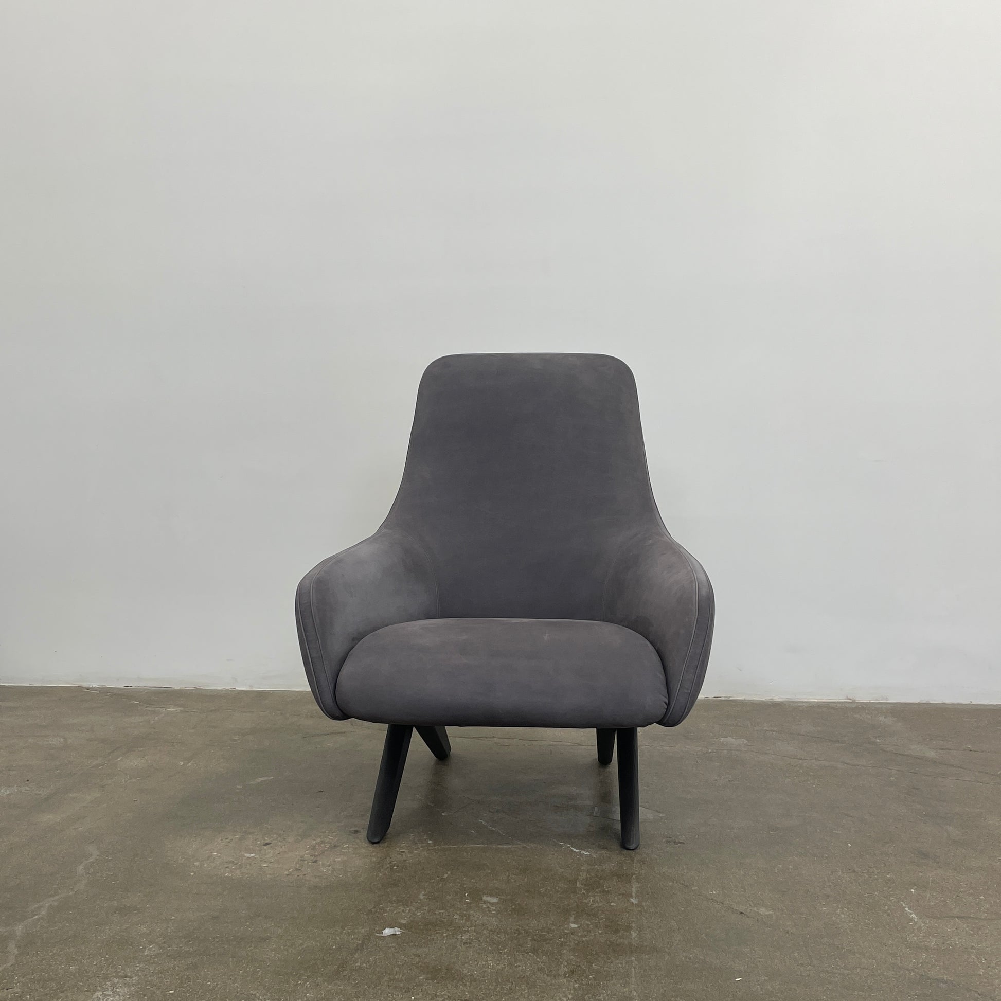 The Poliform Marlon Armchair, featuring a gray finish and sleek, angled wooden legs, exudes modern sophistication against a plain white background.