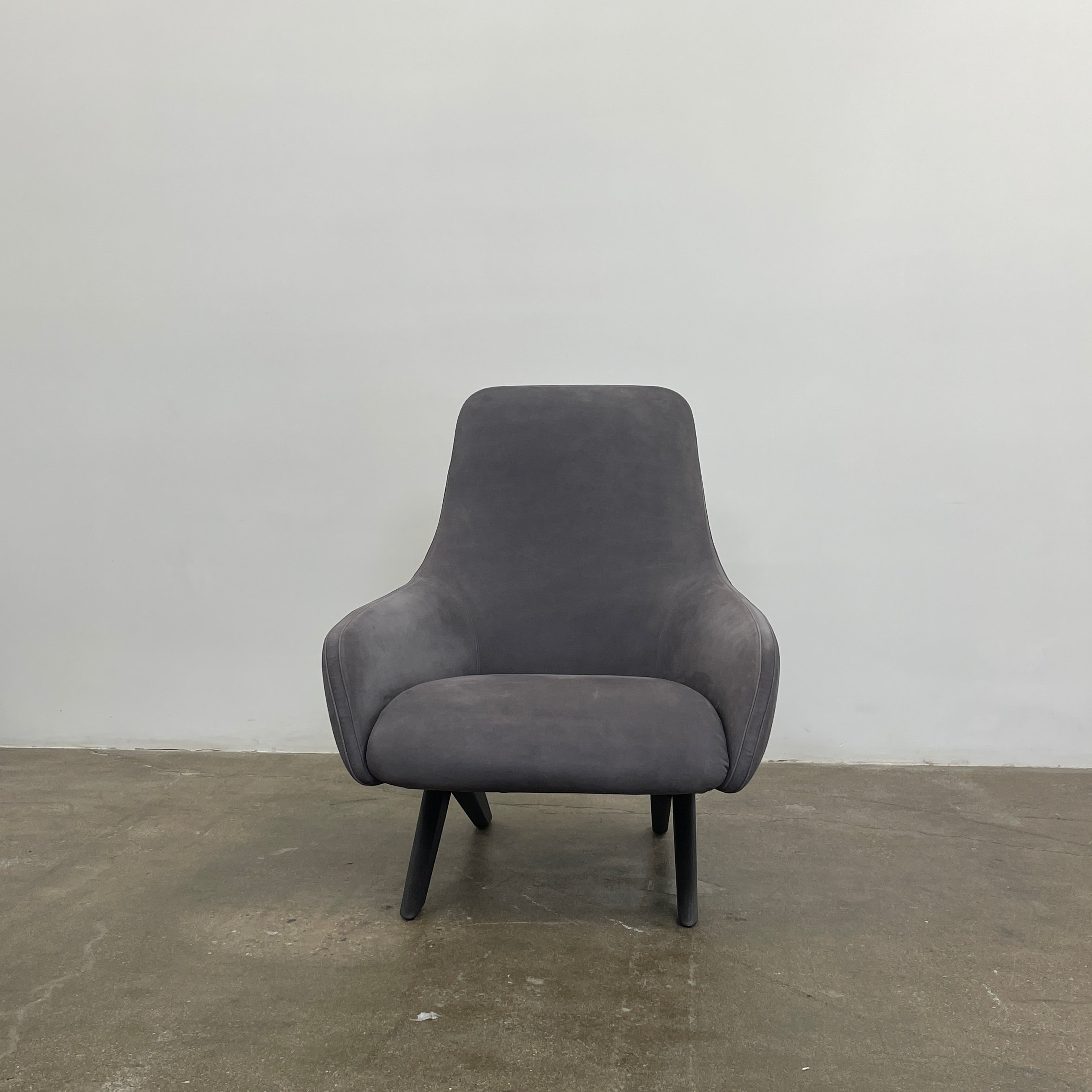 The Poliform Marlon Armchair, featuring a gray finish and sleek, angled wooden legs, exudes modern sophistication against a plain white background.