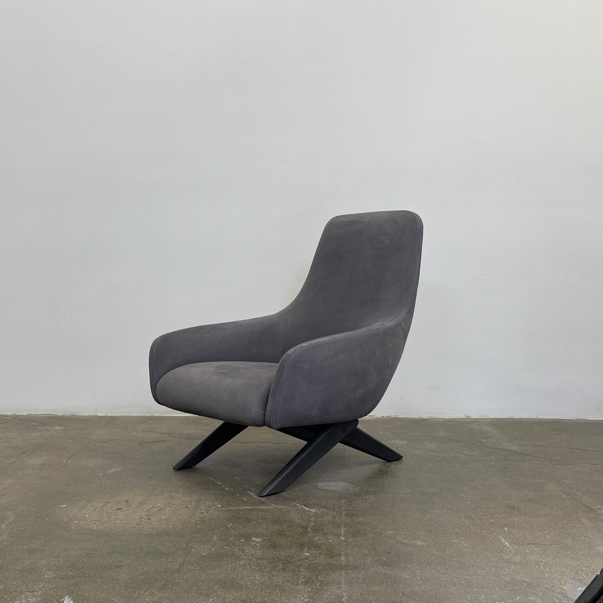 The Poliform Marlon Armchair, featuring a gray finish and sleek, angled wooden legs, exudes modern sophistication against a plain white background.