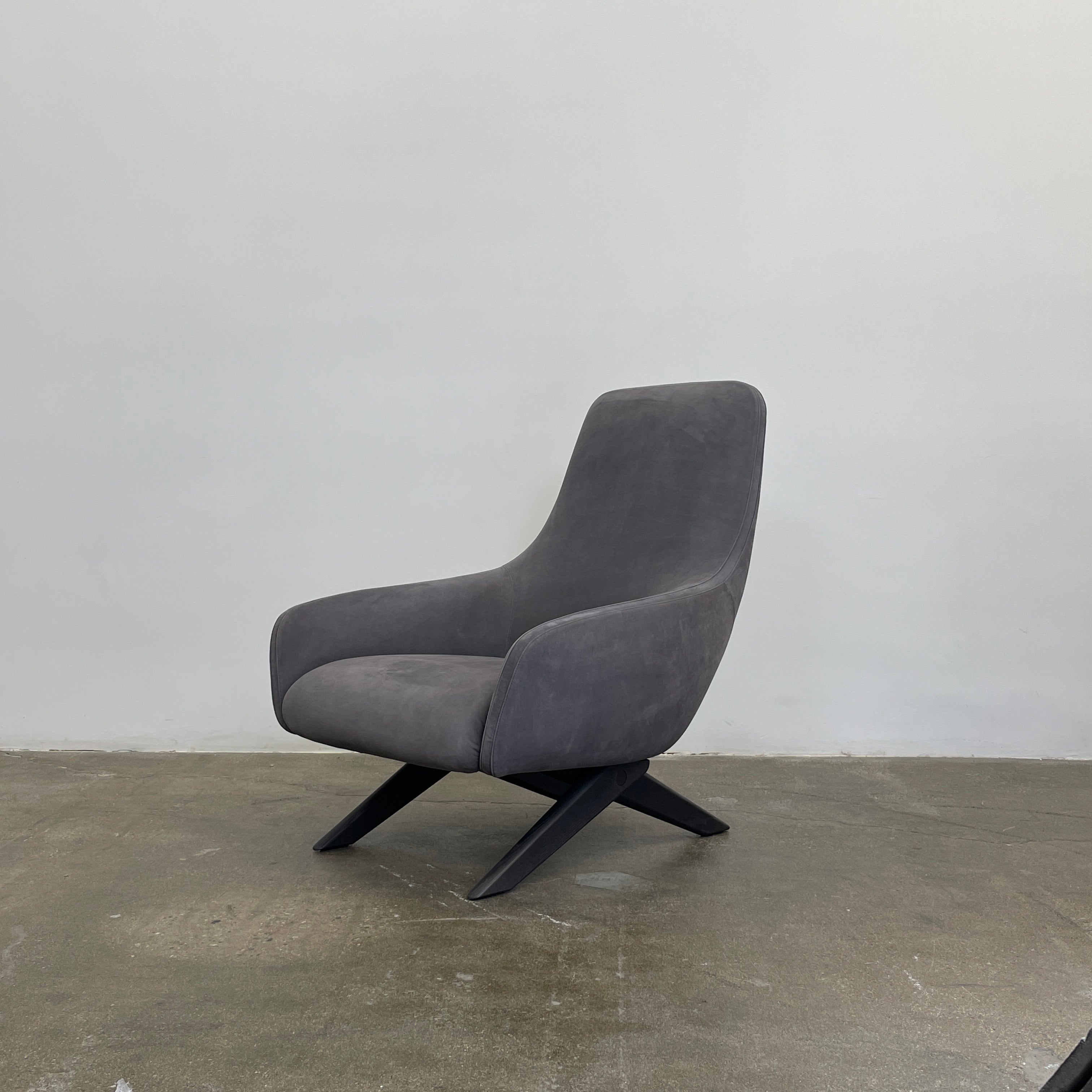 The Poliform Marlon Armchair, featuring a gray finish and sleek, angled wooden legs, exudes modern sophistication against a plain white background.