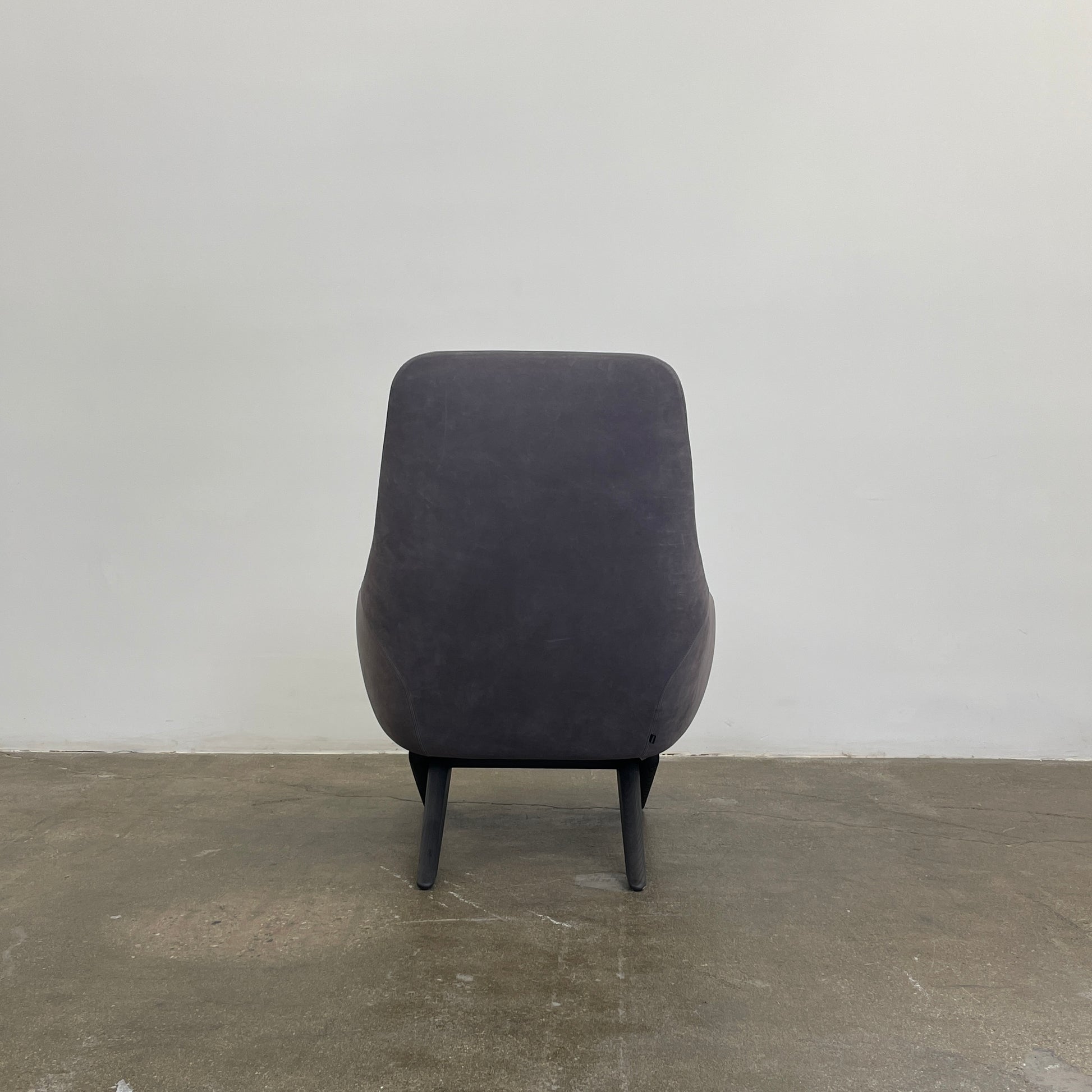 The Poliform Marlon Armchair, featuring a gray finish and sleek, angled wooden legs, exudes modern sophistication against a plain white background.