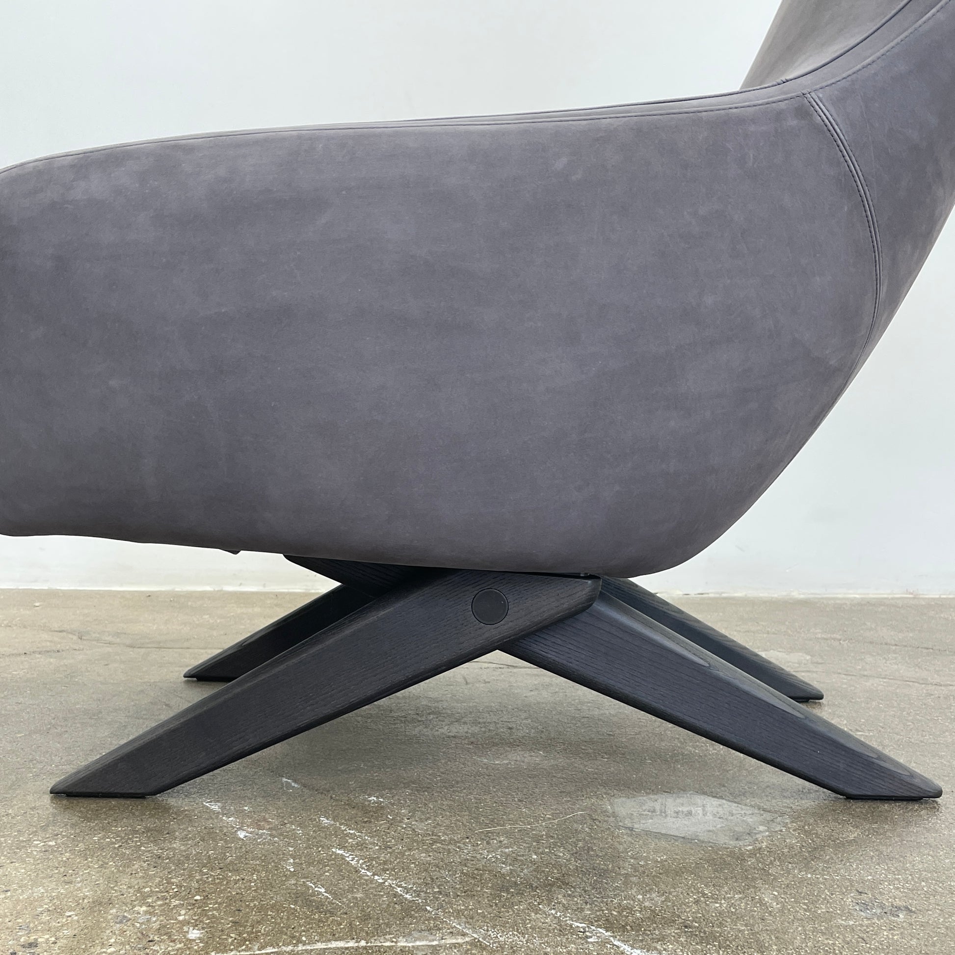 The Poliform Marlon Armchair, featuring a gray finish and sleek, angled wooden legs, exudes modern sophistication against a plain white background.