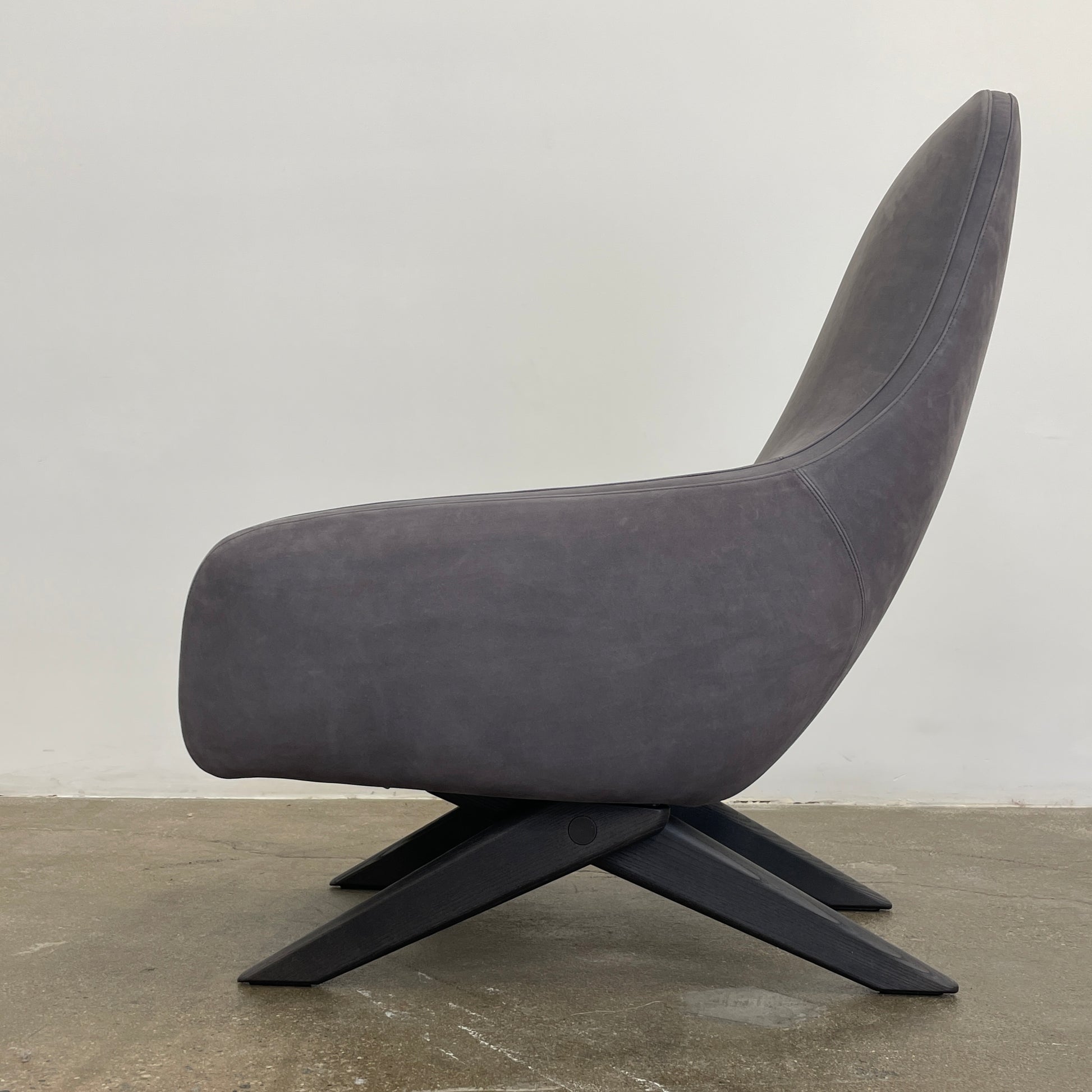 The Poliform Marlon Armchair, featuring a gray finish and sleek, angled wooden legs, exudes modern sophistication against a plain white background.