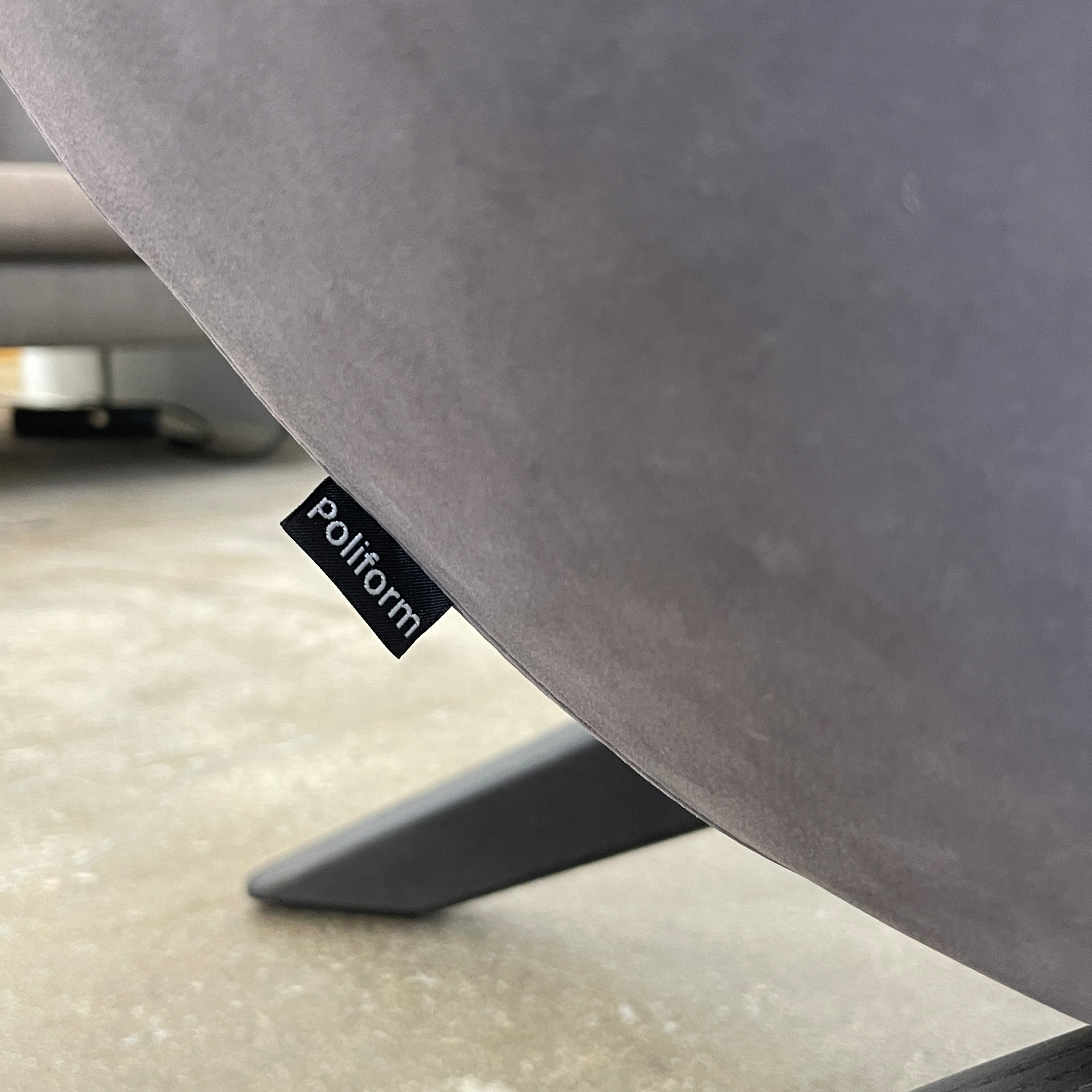 The Poliform Marlon Armchair, featuring a gray finish and sleek, angled wooden legs, exudes modern sophistication against a plain white background.