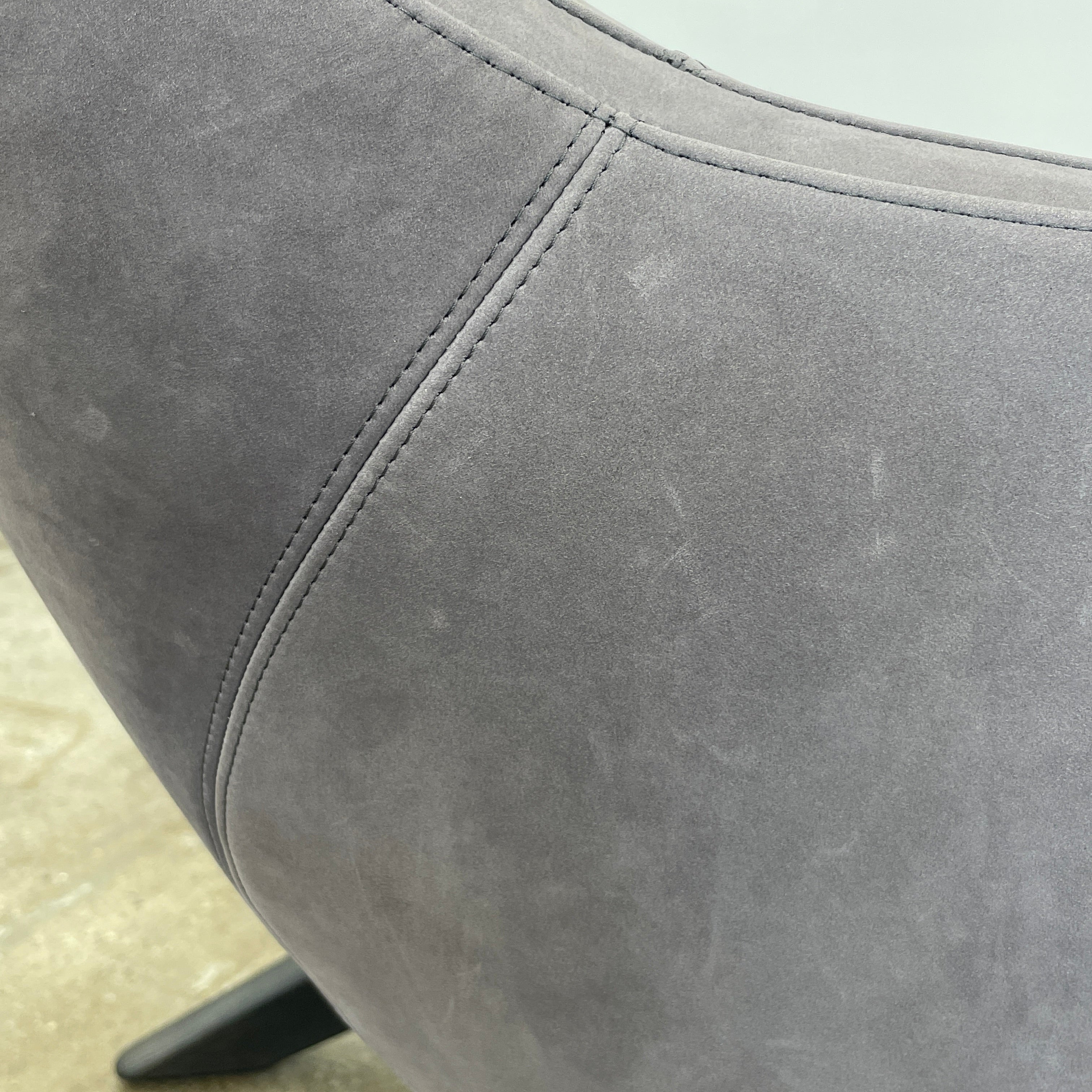 The Poliform Marlon Armchair, featuring a gray finish and sleek, angled wooden legs, exudes modern sophistication against a plain white background.