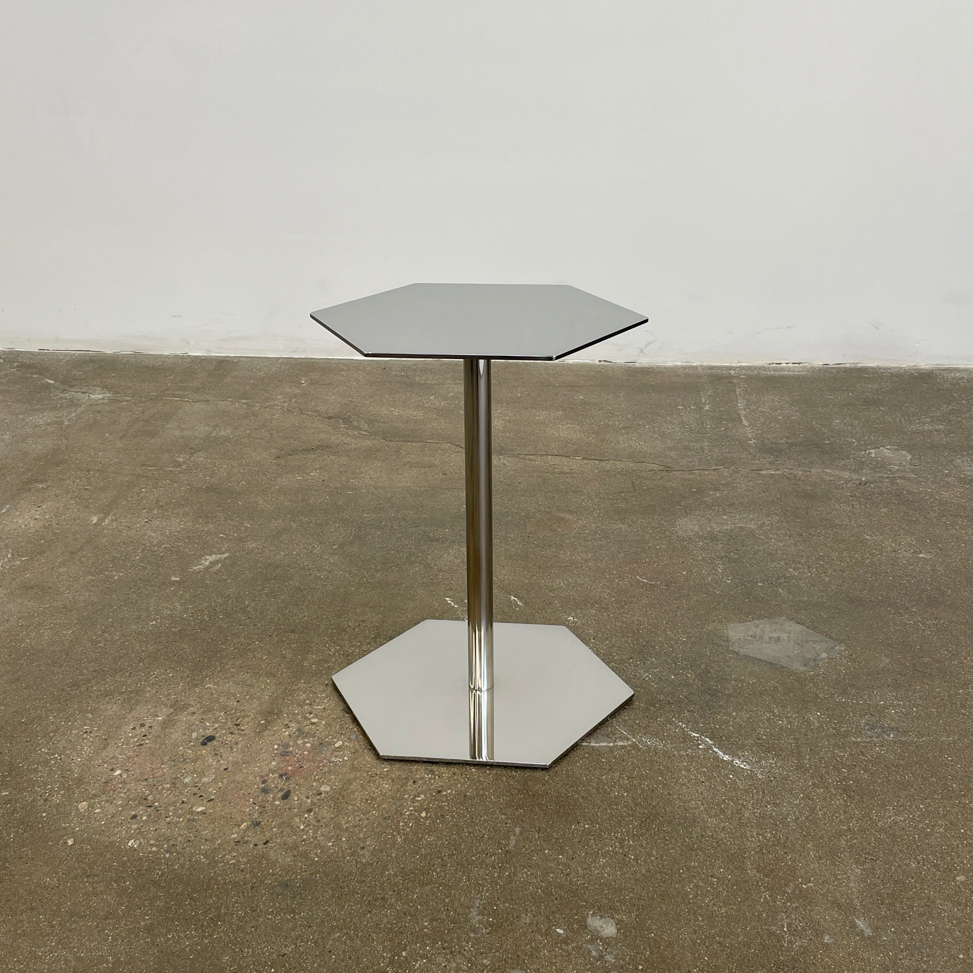 The Minotti Brisley Side Table by Rodolfo Dordoni features a stylish hexagonal metal surface supported by a central stand that flows into a matching base.