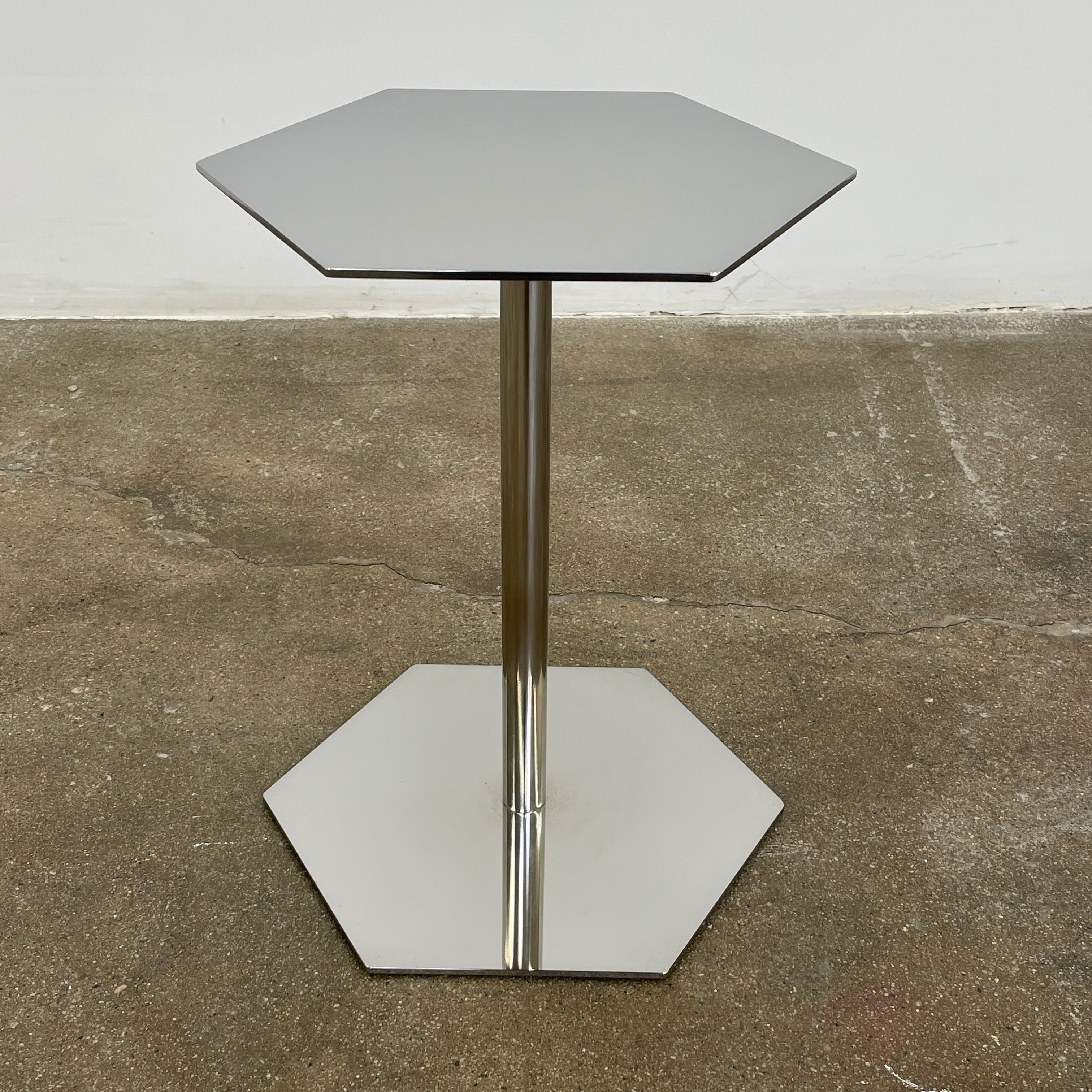 The Minotti Brisley Side Table by Rodolfo Dordoni features a stylish hexagonal metal surface supported by a central stand that flows into a matching base.